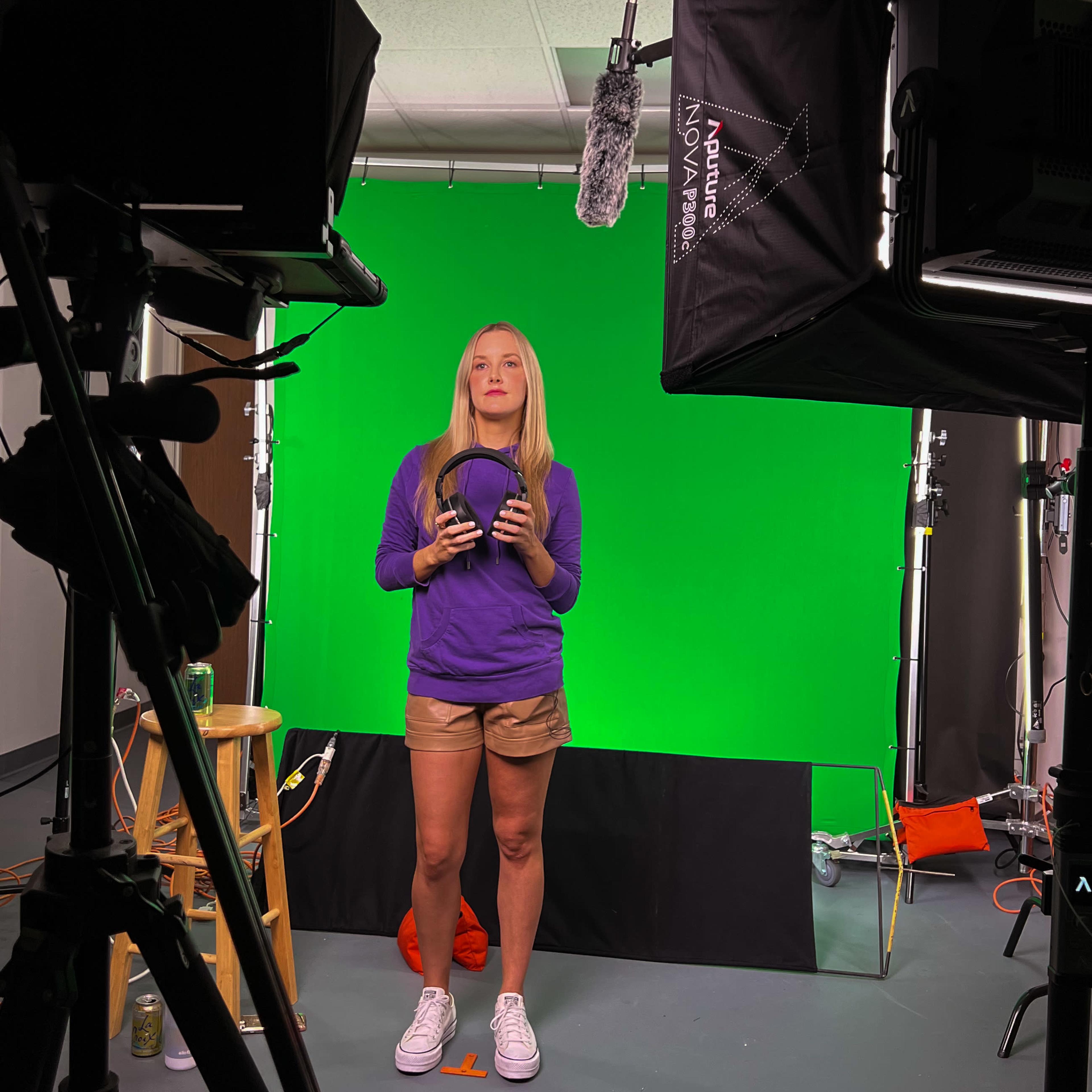 A person stands in front of a green screen, holding a basketball, while surrounded by studio equipment including cameras and lighting.