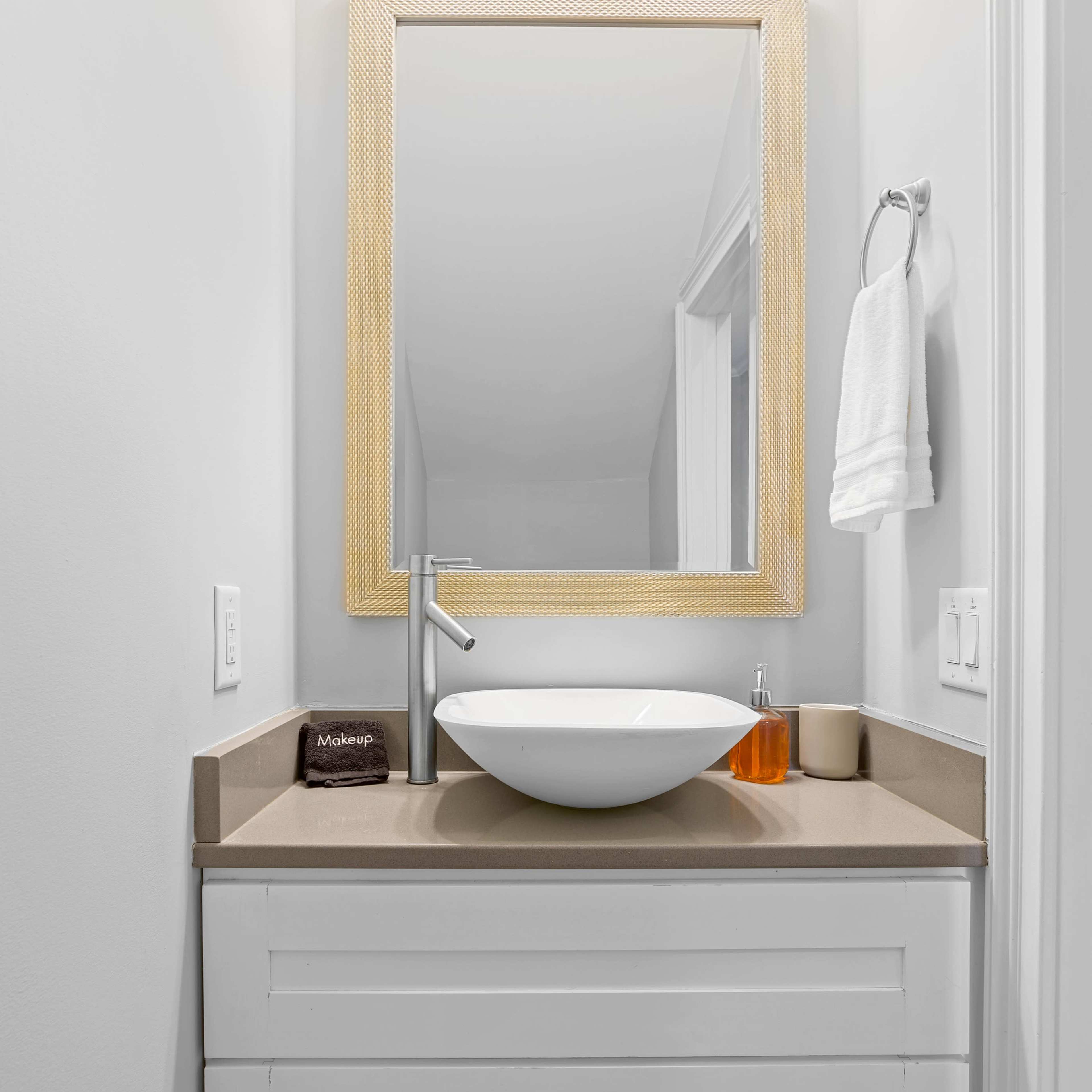 A modern bathroom with a white vanity, a round vessel sink, and a lighted mirror above it.