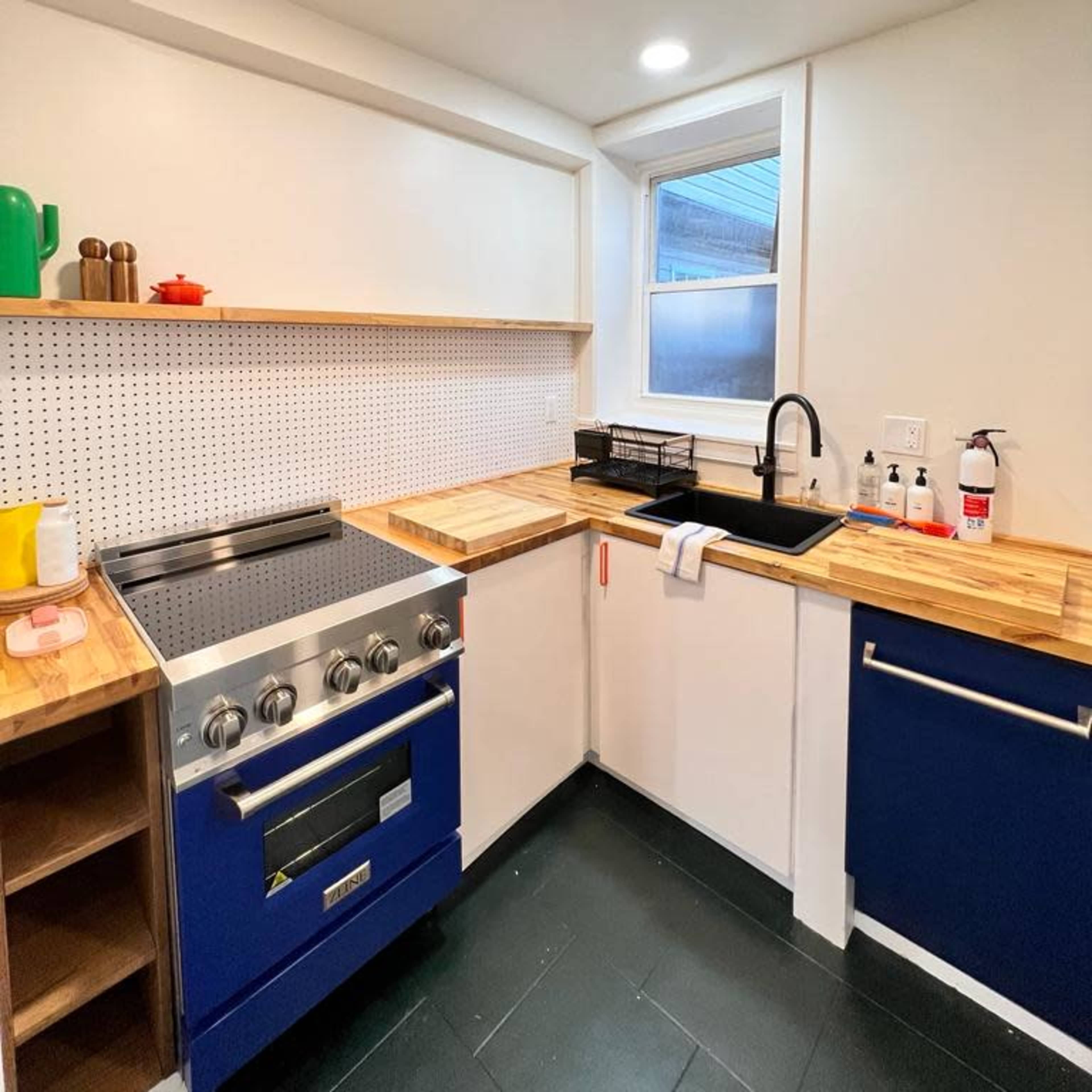 A modern kitchen with navy blue cabinets, wooden countertops, and a stainless steel stove, featuring a black sink beneath a window.