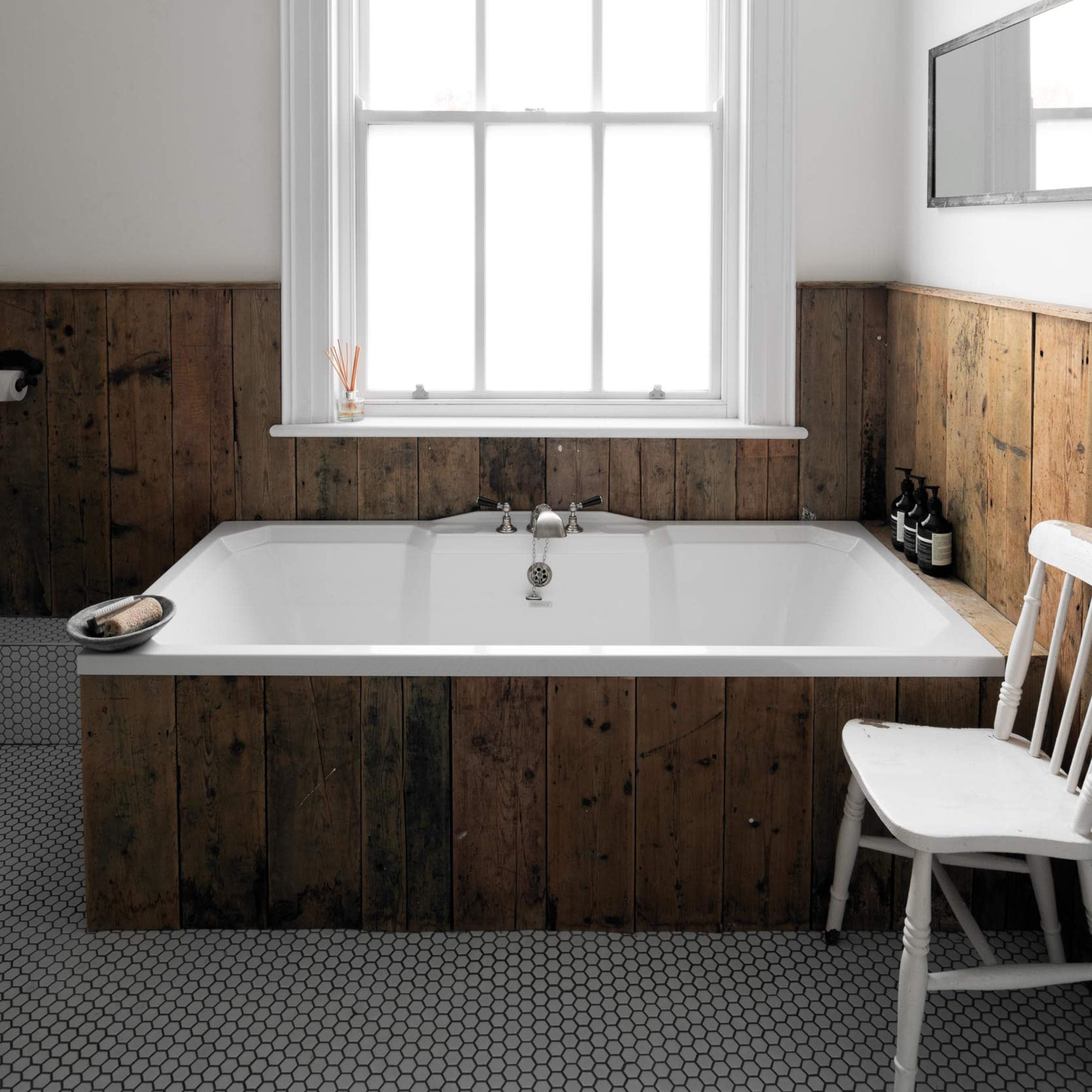 A rectangular white bathtub set against a wall with wooden paneling and a large window above it.