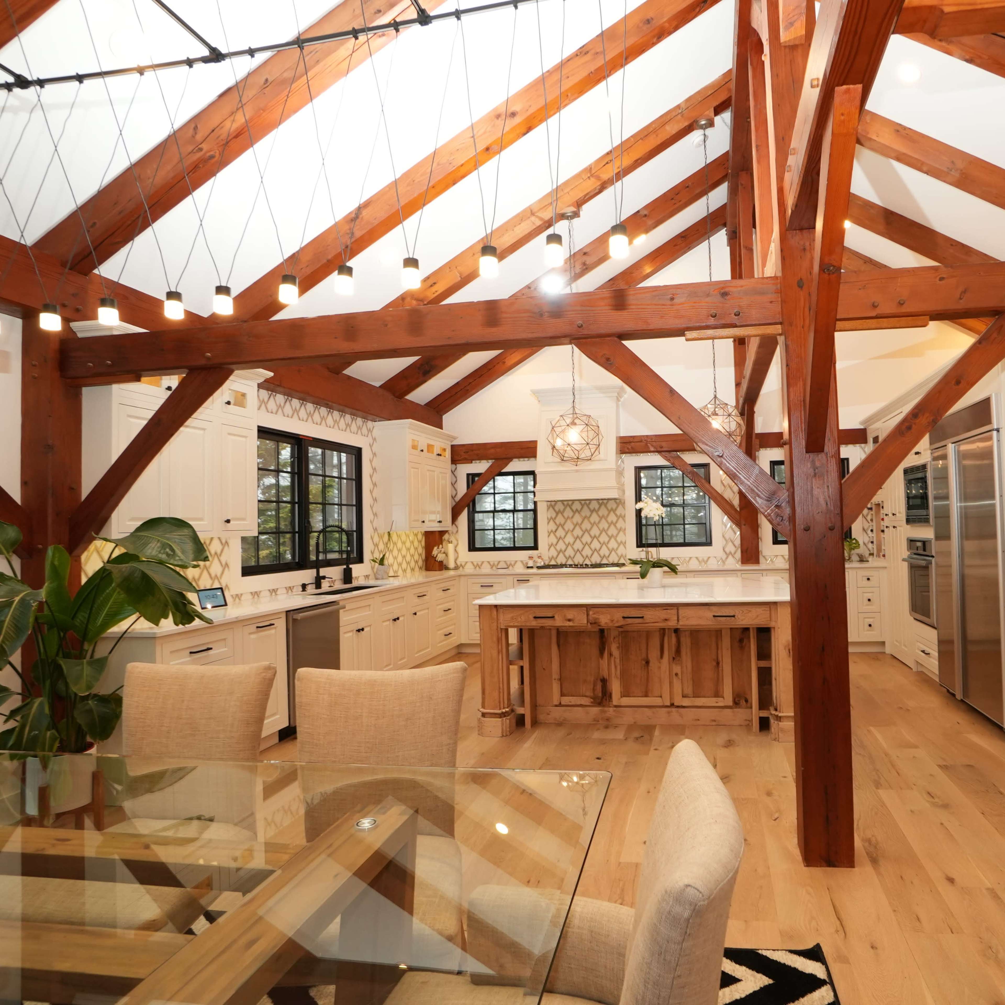 A spacious kitchen with wooden beams, modern appliances, and a dining area featuring a glass table and beige chairs.