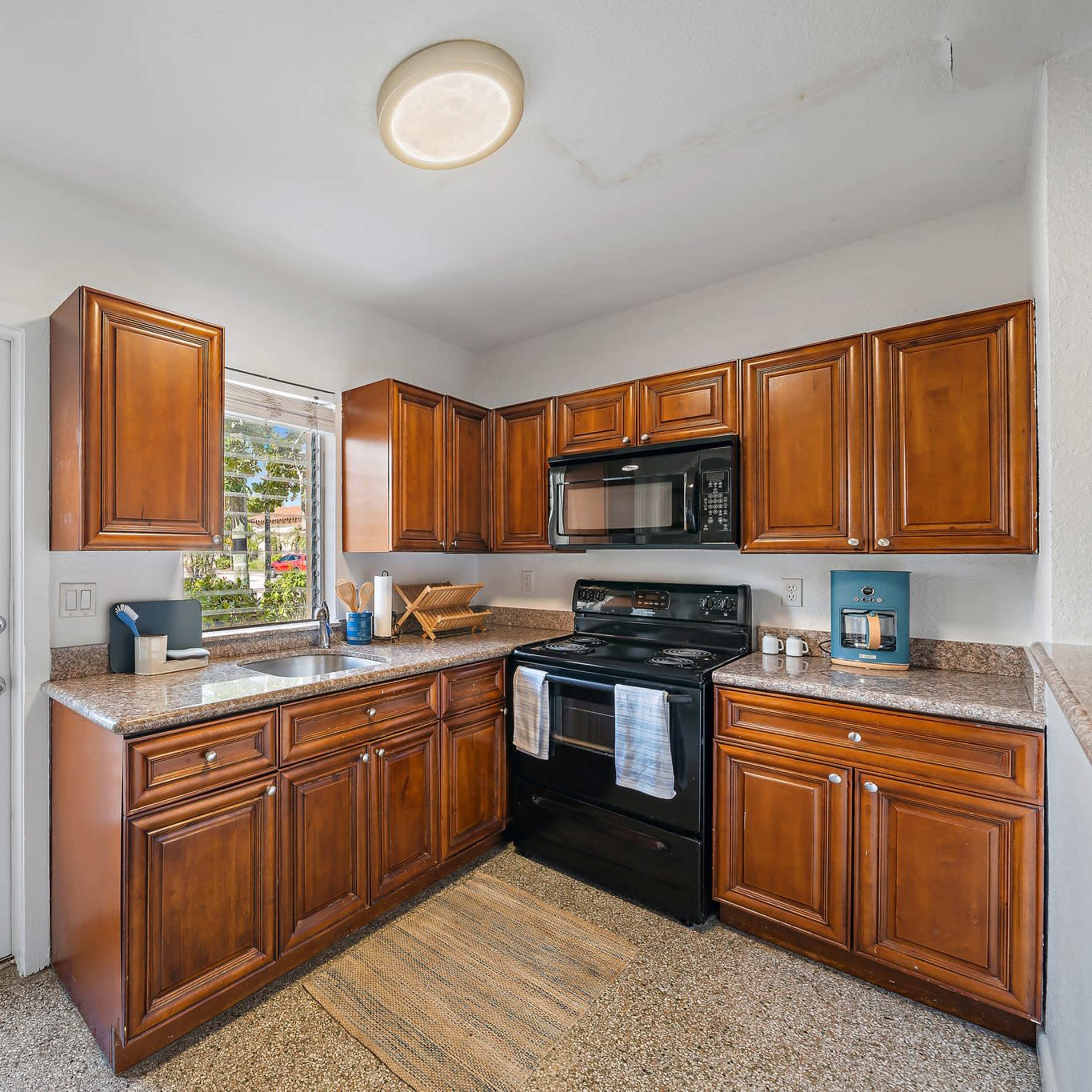 The kitchen features brown wooden cabinets, a black stove and microwave, and a countertop with a window overlooking the exterior.