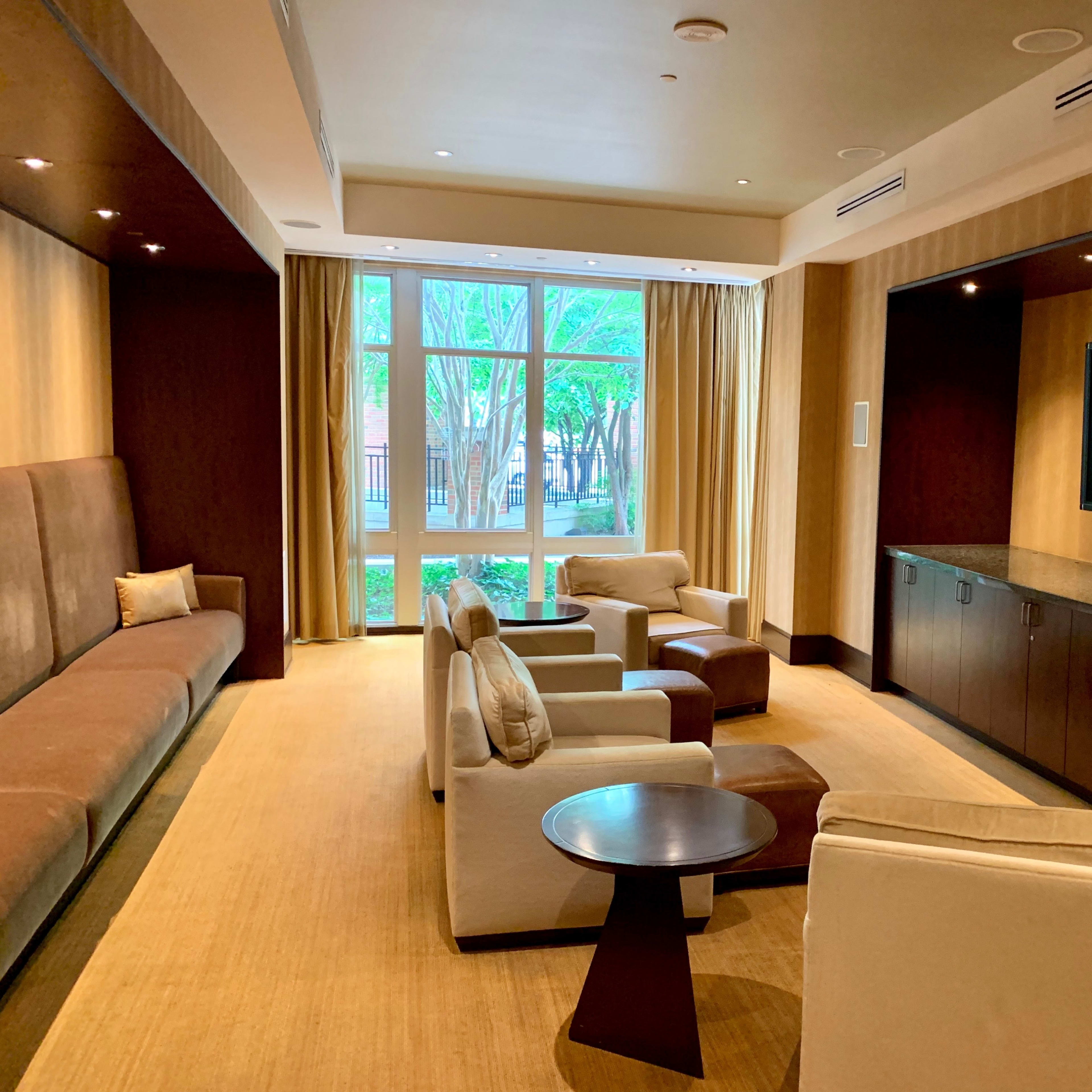 A modern living room with a long sofa, several armchairs, a coffee table, and a flat-screen TV, all oriented around large windows letting in natural light.
