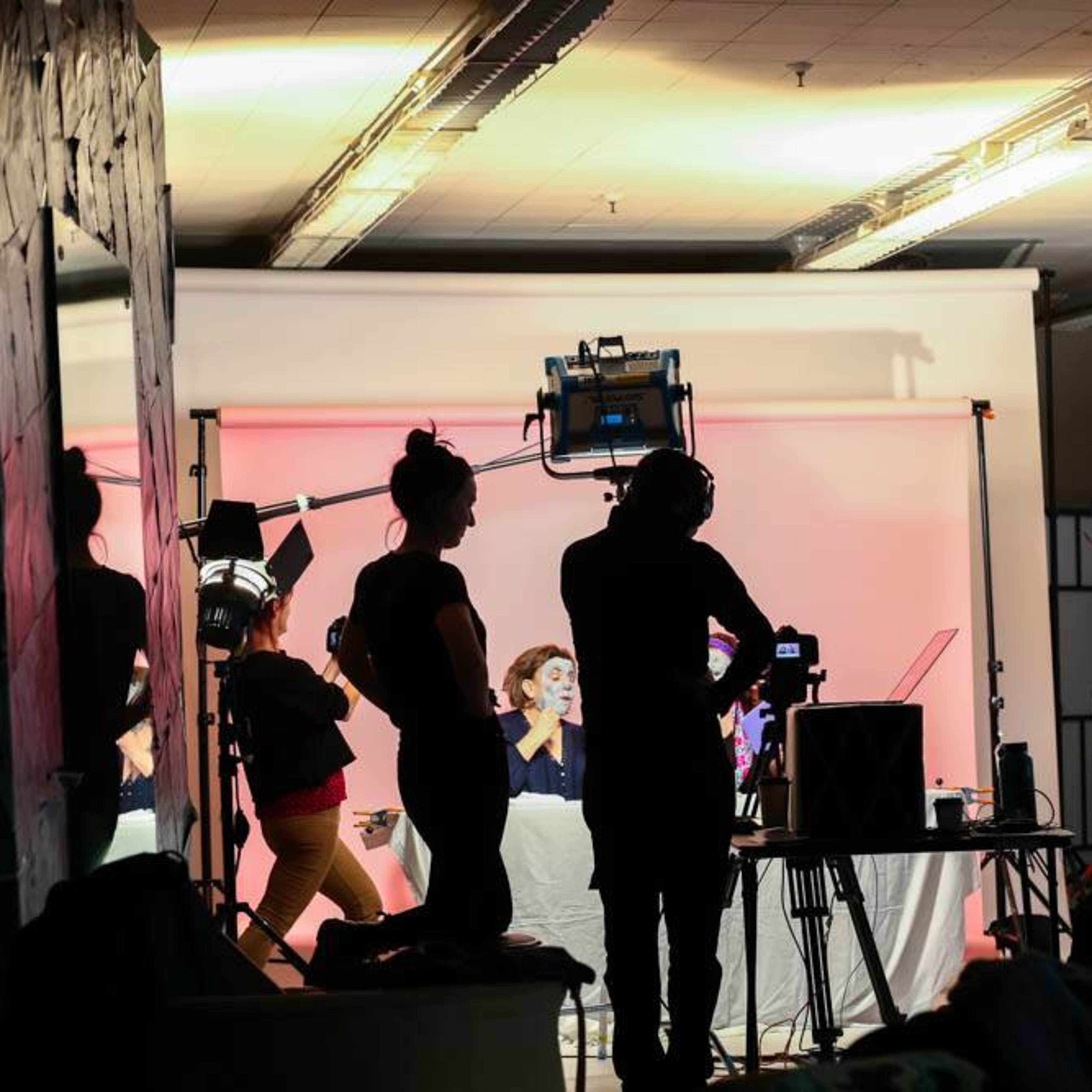 A film crew is silhouetted against a backdrop while setting up lights and equipment for a shoot.