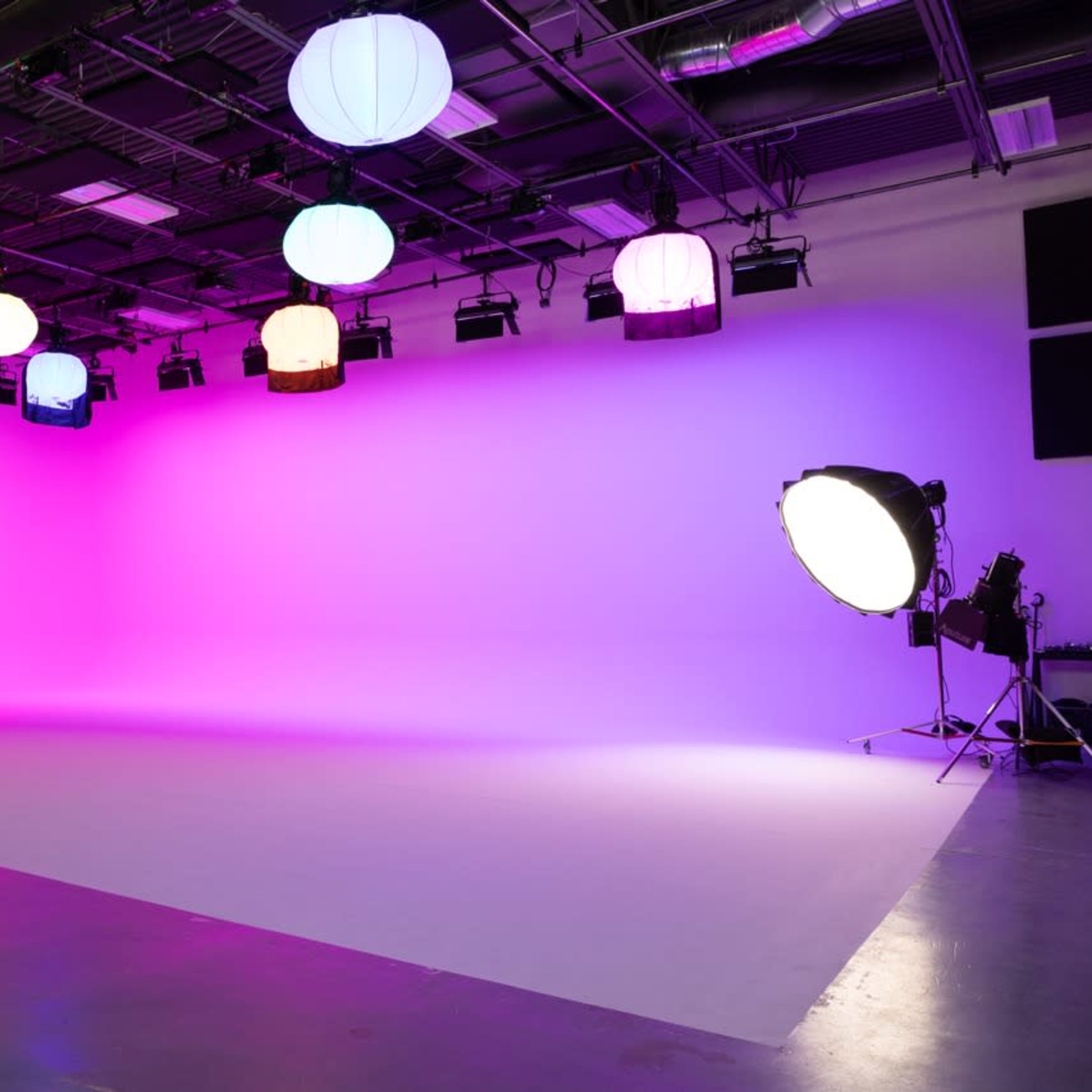An empty studio space with colorful hanging lanterns and a large light source aimed at a plain backdrop.