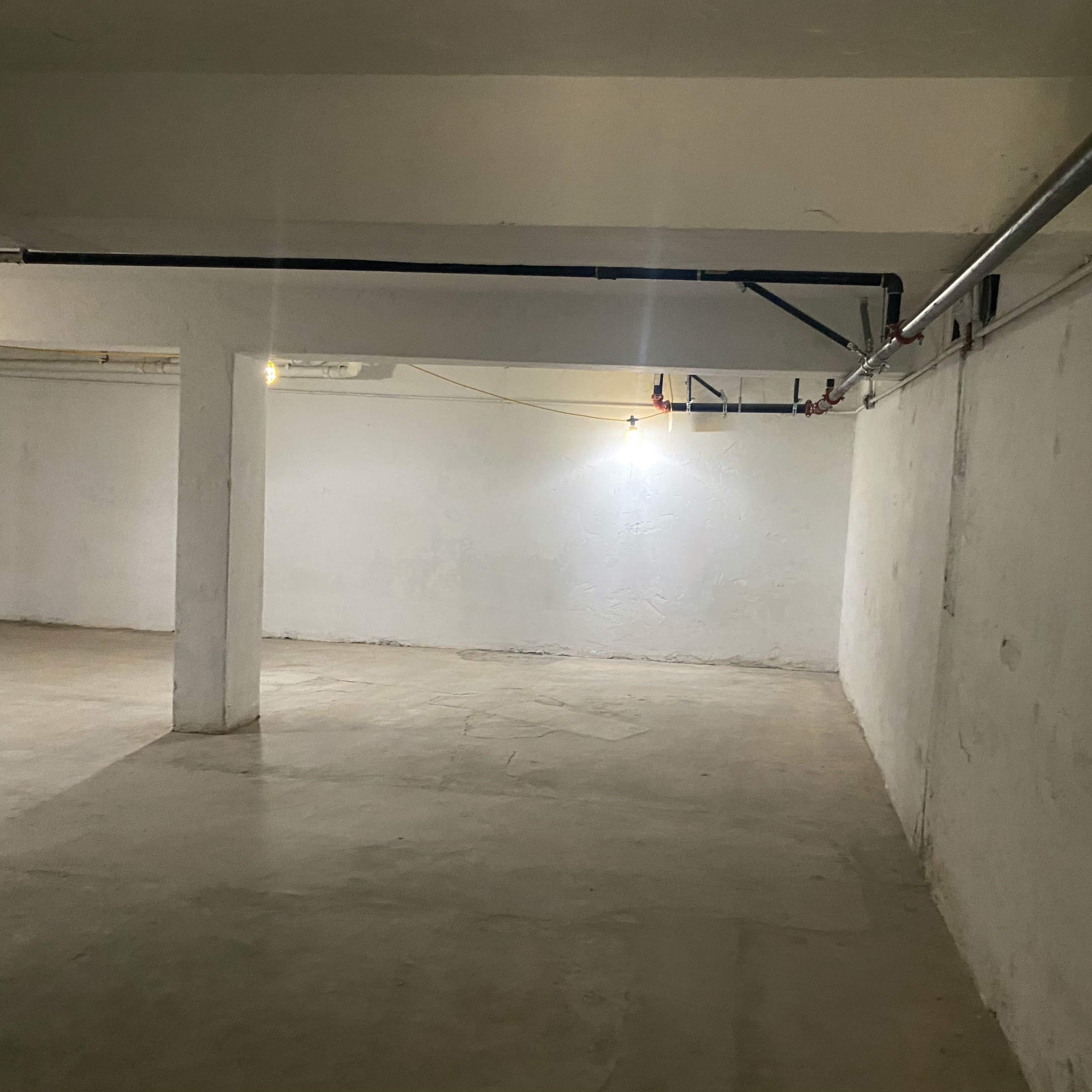 A spacious, empty basement with bare concrete floors and exposed pipes along the ceiling.
