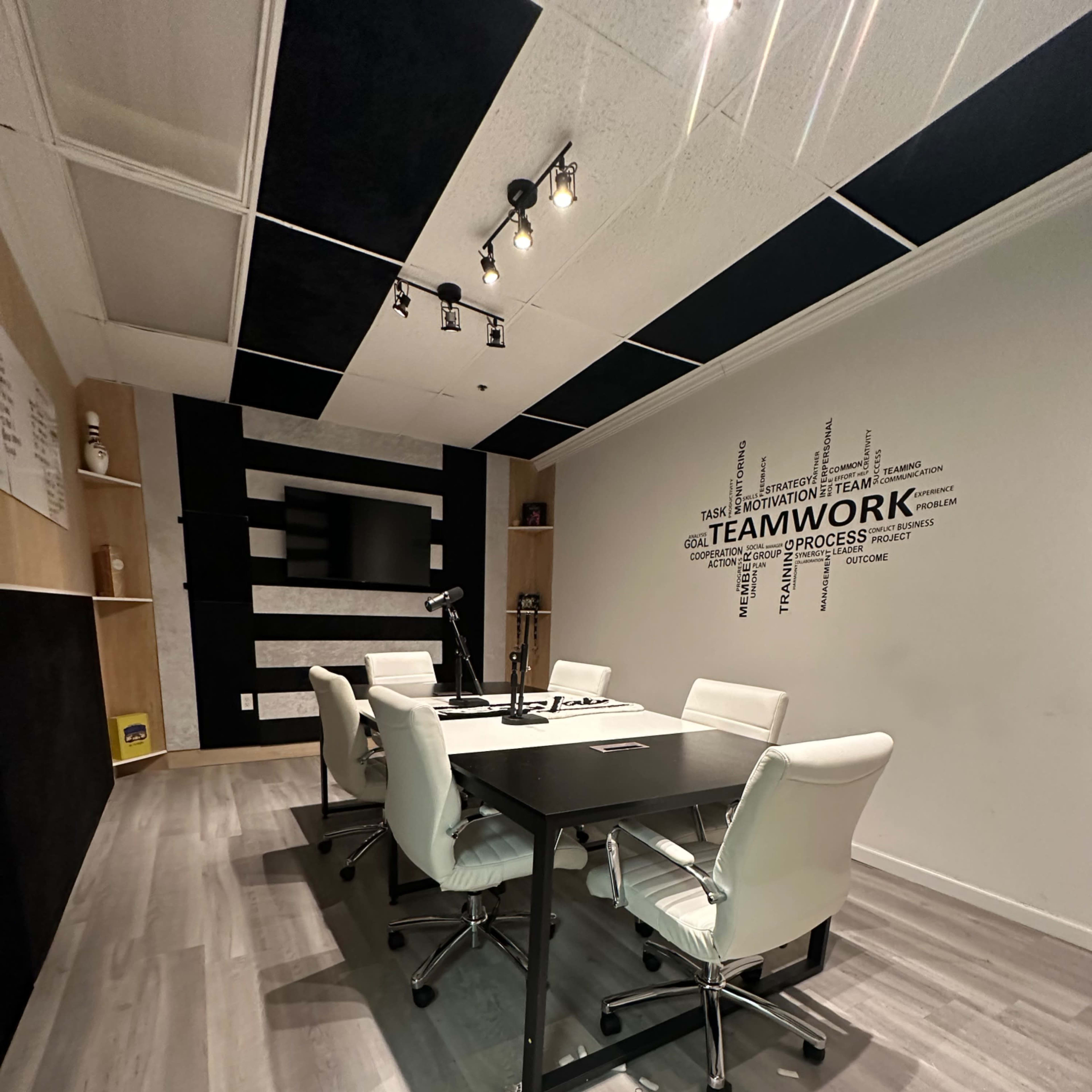 A modern conference room with a black and white color scheme, featuring a rectangular table surrounded by white chairs and a wall decorated with the word "TEAMWORK."