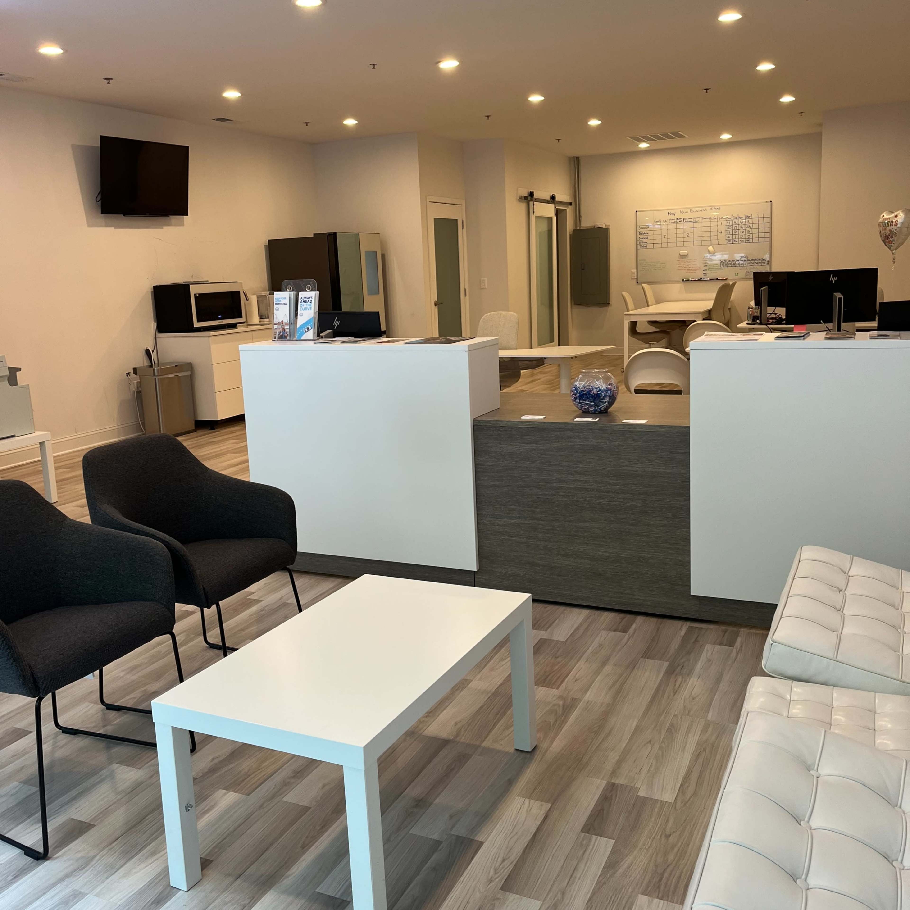 A modern reception area with seating, a table, and a desk space in a well-lit office environment.