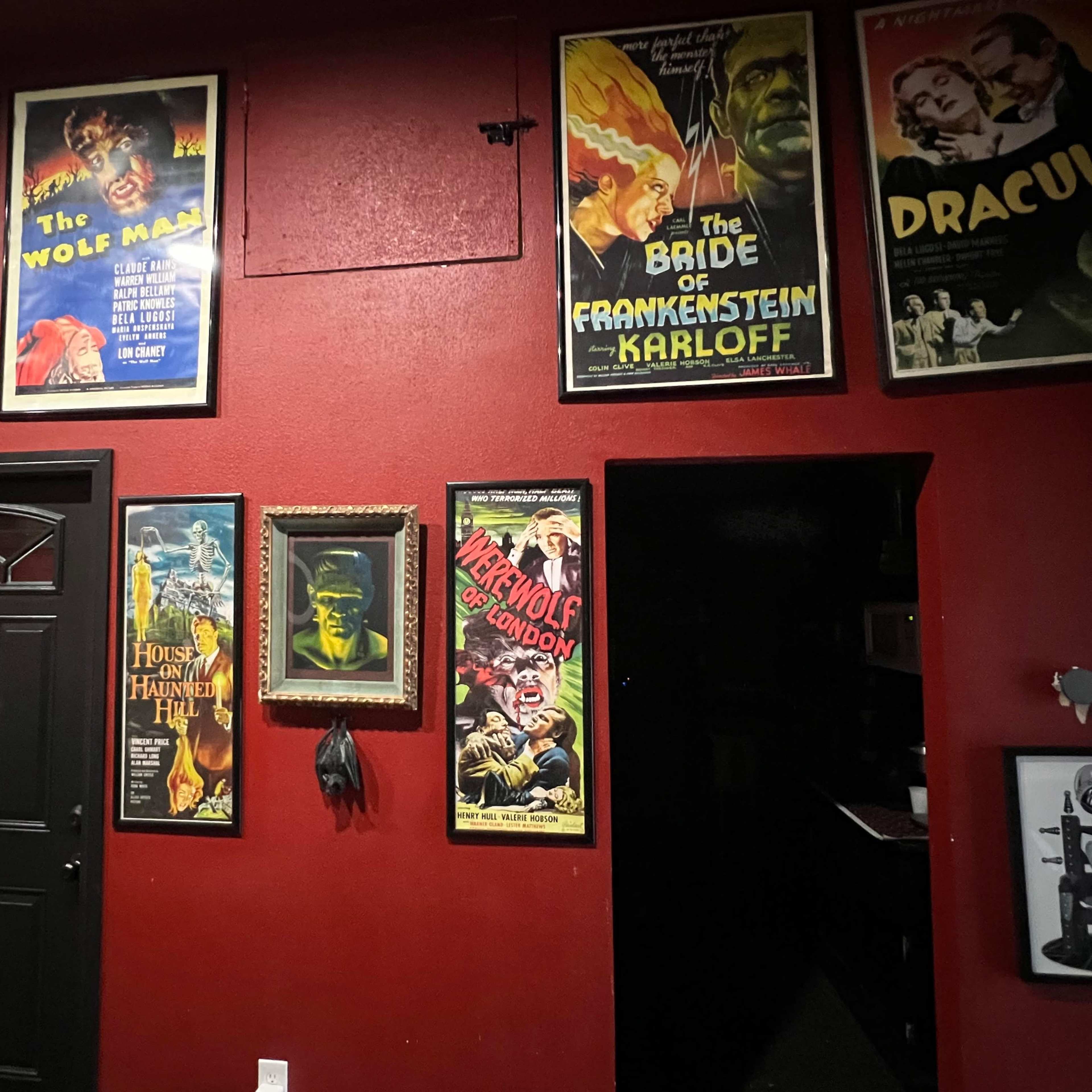 A red wall adorned with vintage horror movie posters featuring titles like "Dracula," "The Wolf Man," and "The Bride of Frankenstein."