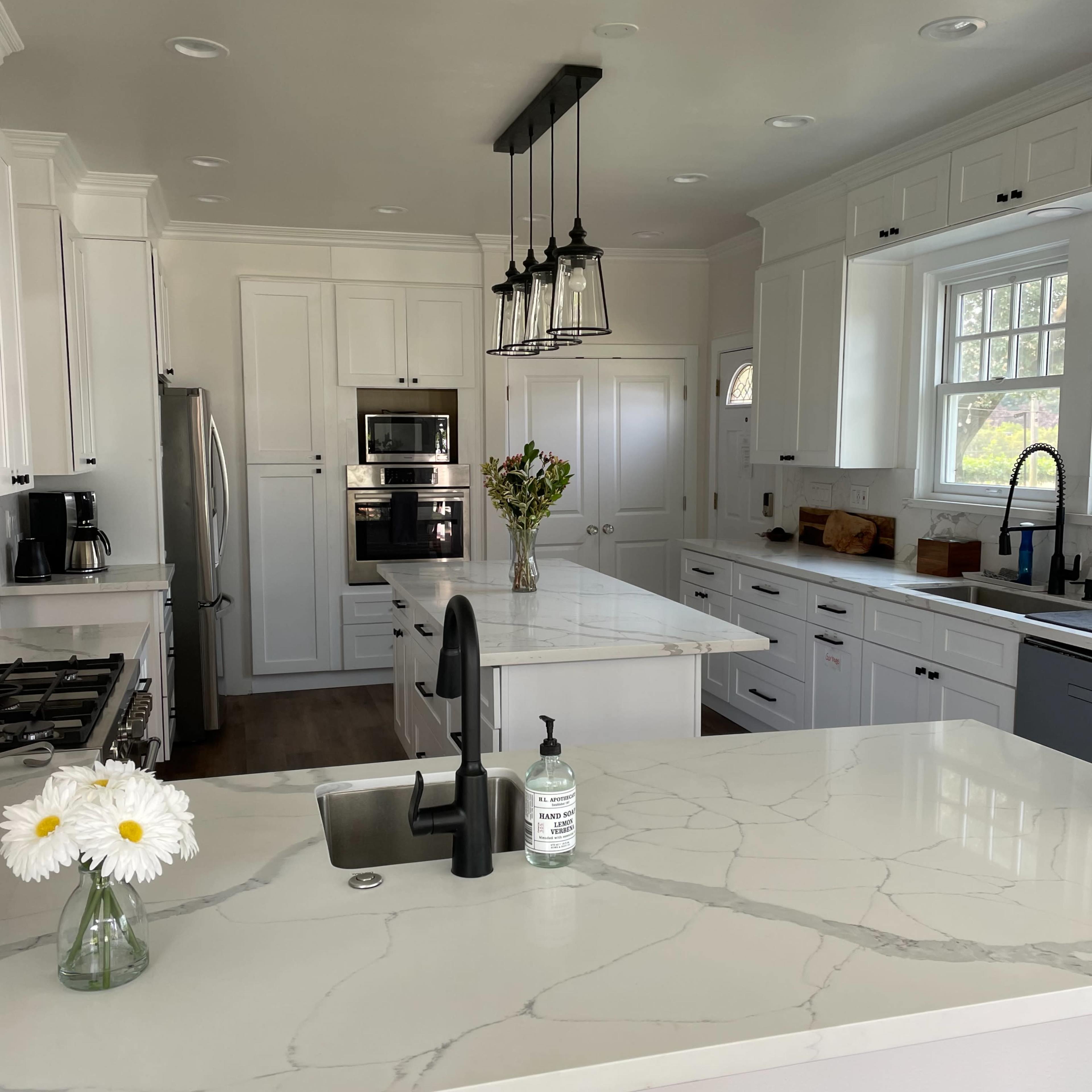 A modern kitchen with white cabinetry, a marble countertop, and a central island featuring a black faucet and sink.