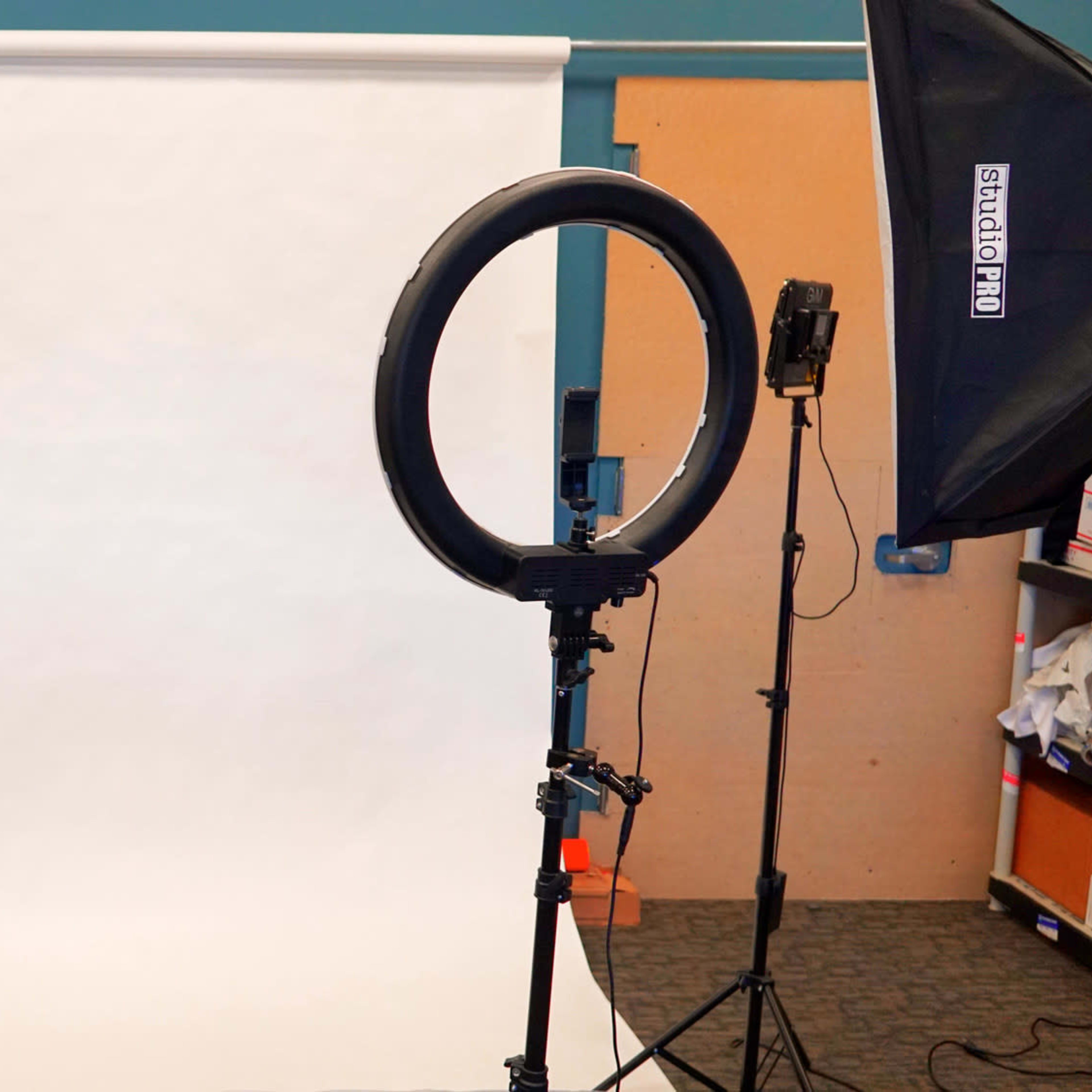 A photography setup with a white backdrop, a ring light, and two studio lights on tripods.