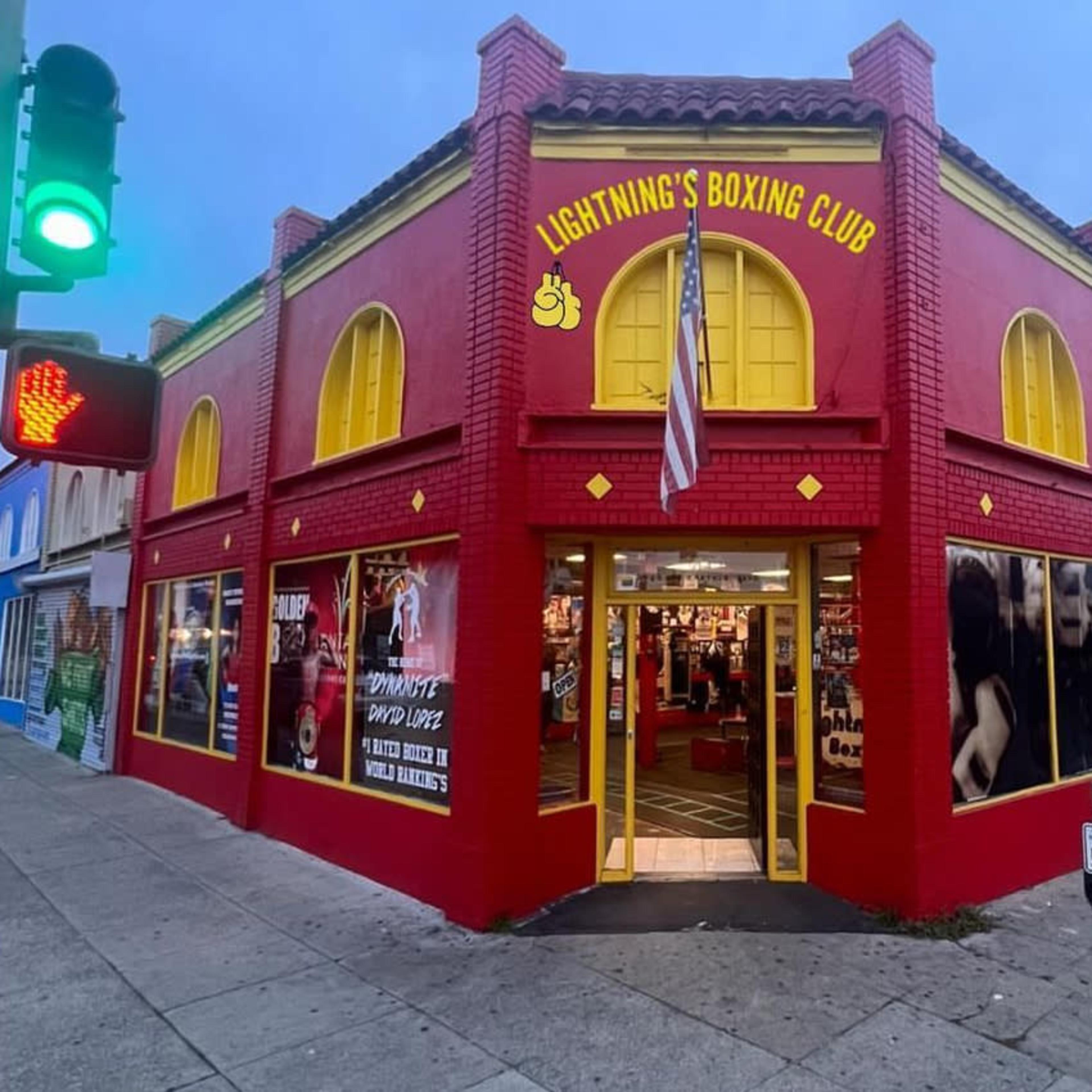 A brightly painted red building with the sign "Lightning's Boxing Club" and large black-and-white photographs of boxers on its exterior.