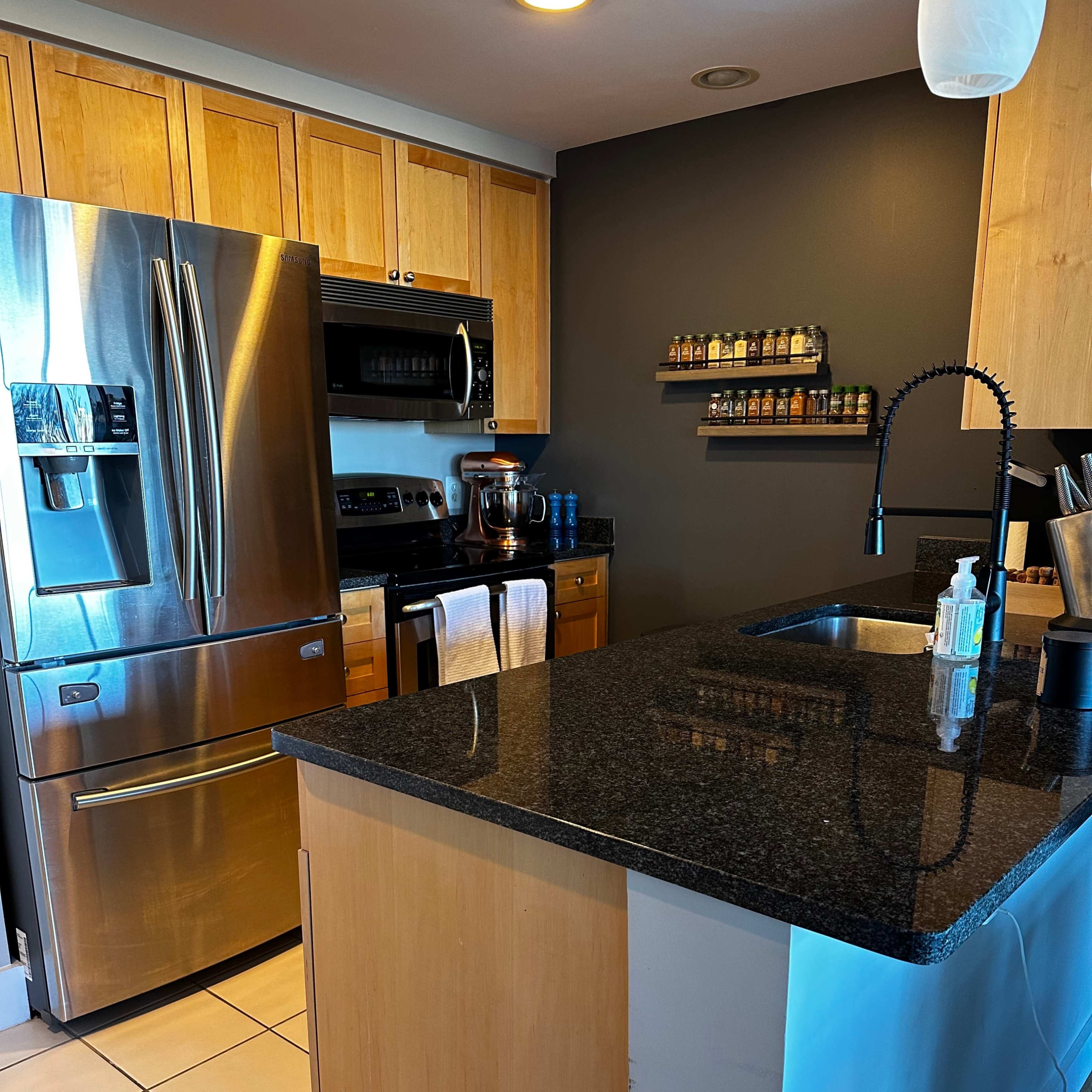 A modern kitchen with stainless steel appliances, wooden cabinetry, and a granite countertop island.