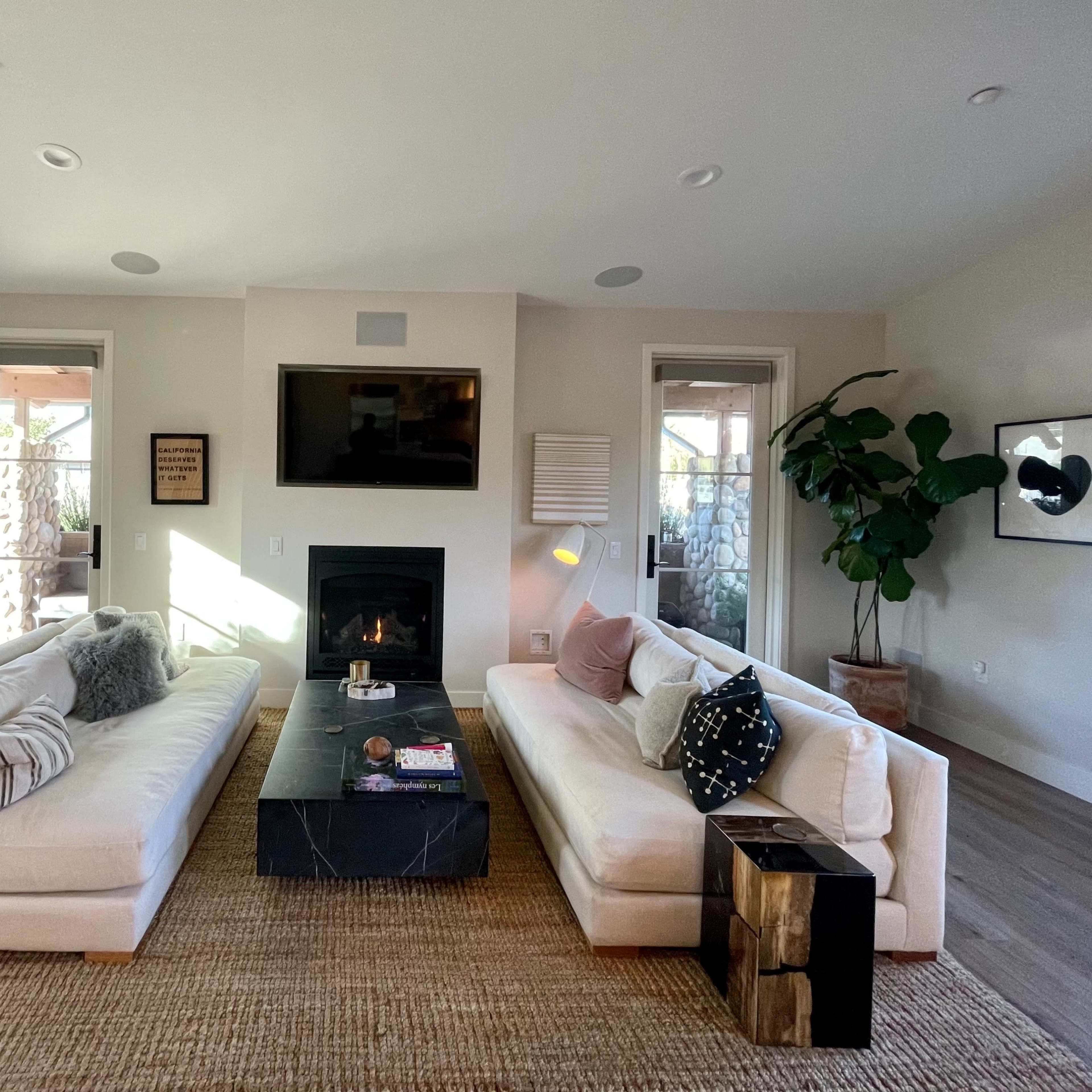 The living room features two white sofas facing each other, a black coffee table in the center, and a fireplace against a light-colored wall.