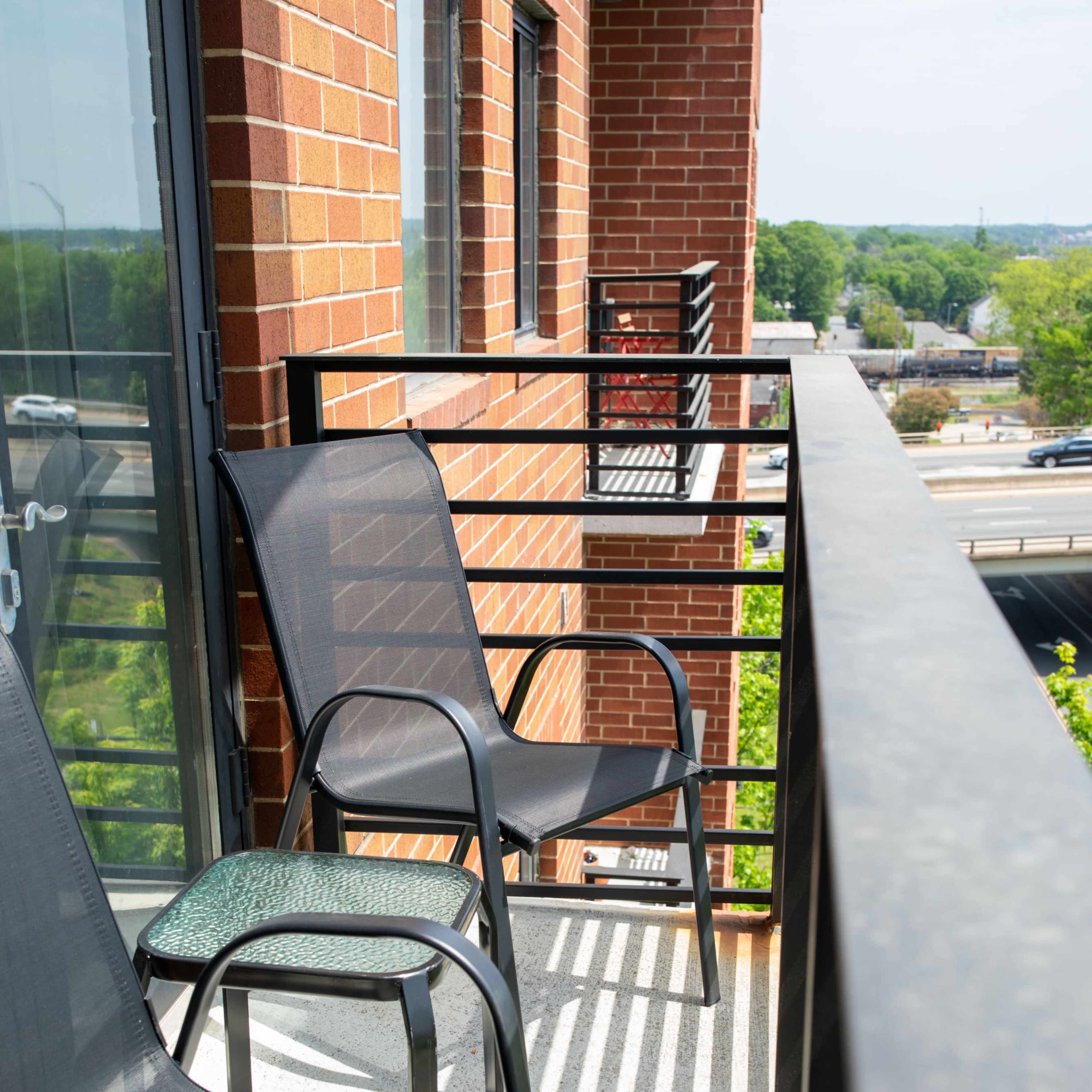 Two black chairs sit on a balcony with a view of a road and trees in the background.