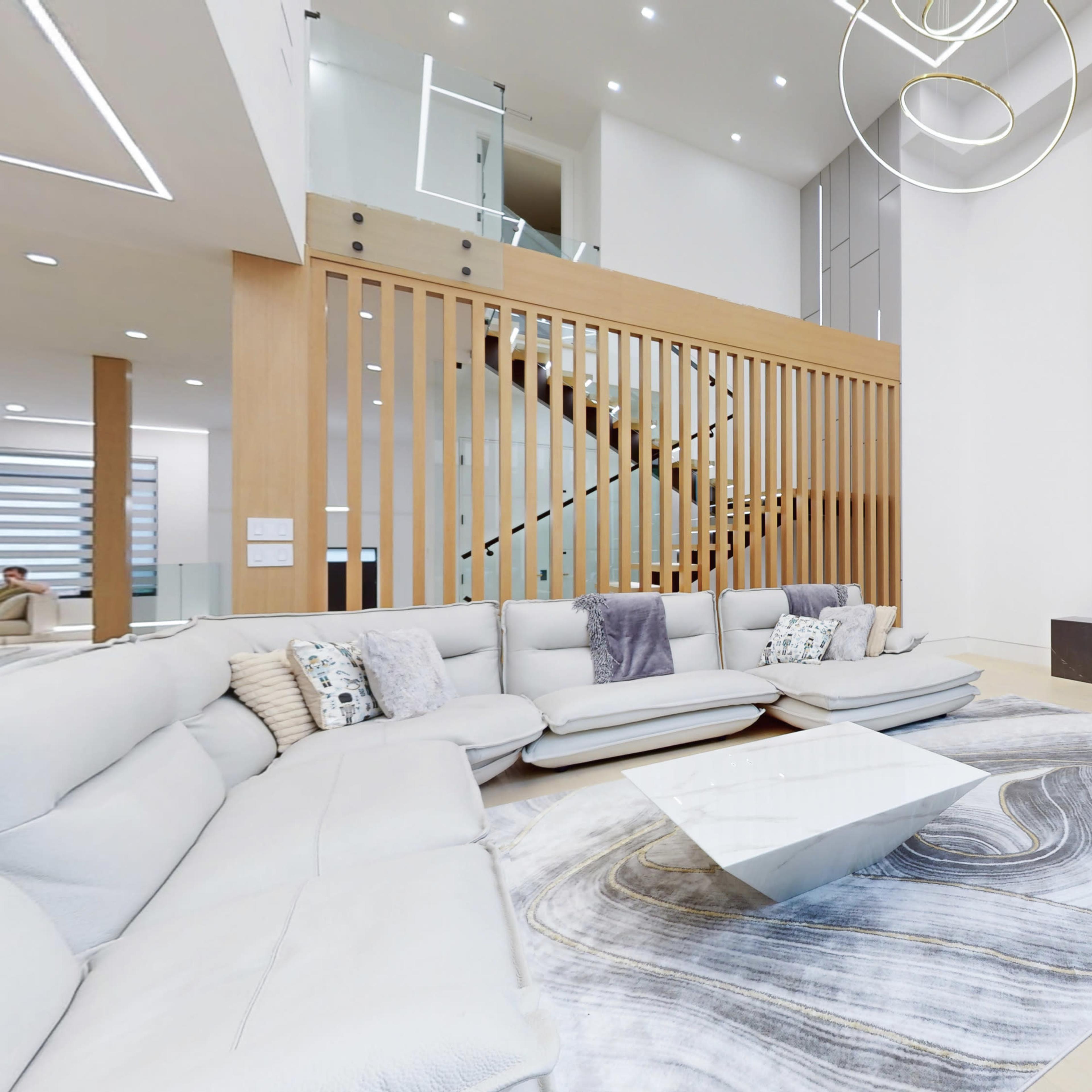 A spacious modern living room with a large sectional sofa, a geometric coffee table, and a marble accent wall featuring a mounted television and an integrated fireplace.
