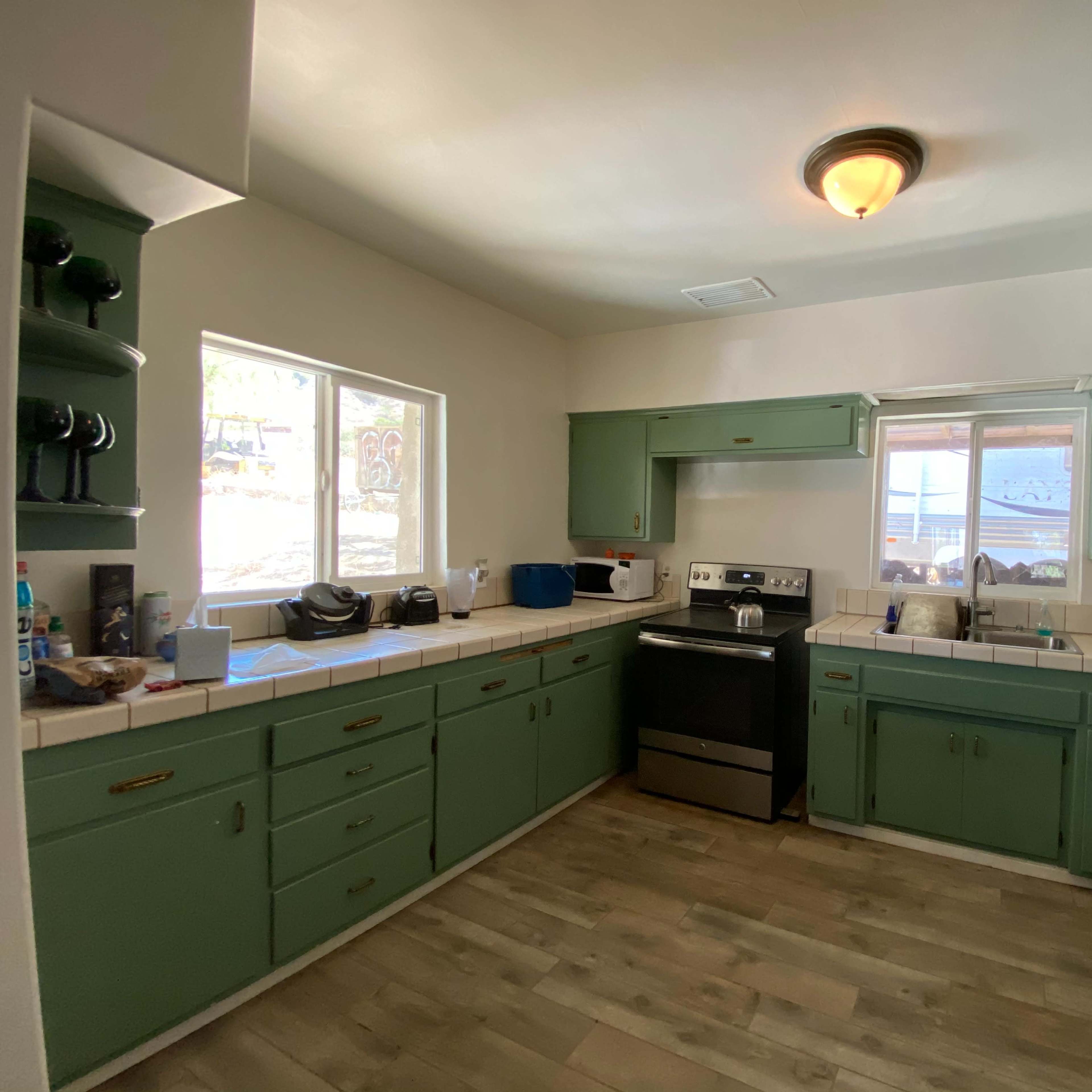 A sparsely furnished kitchen features green cabinets, white countertops, and a stainless steel stove.