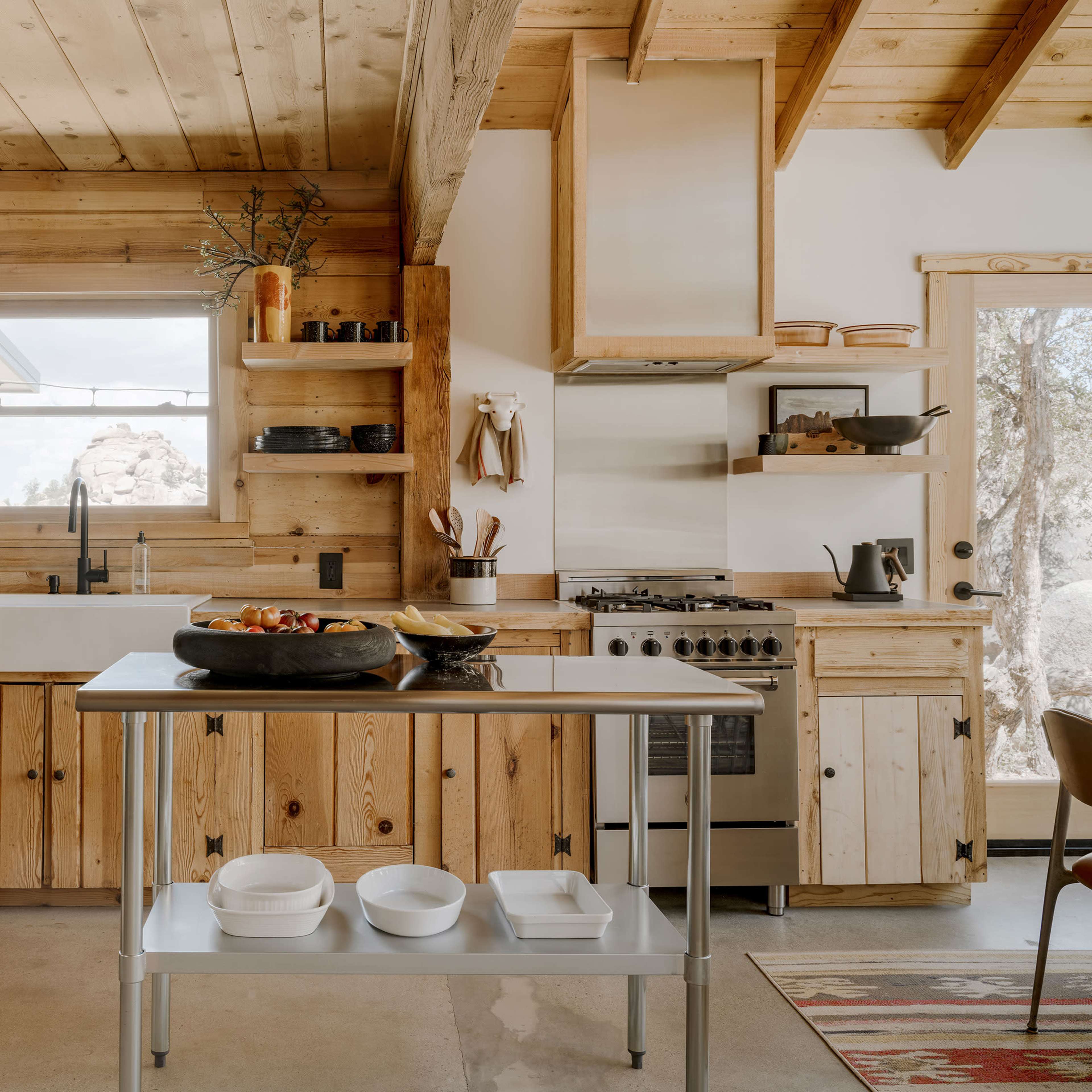 The kitchen features wooden cabinetry, a stainless steel refrigerator, and an island with white dishware on a concrete floor.