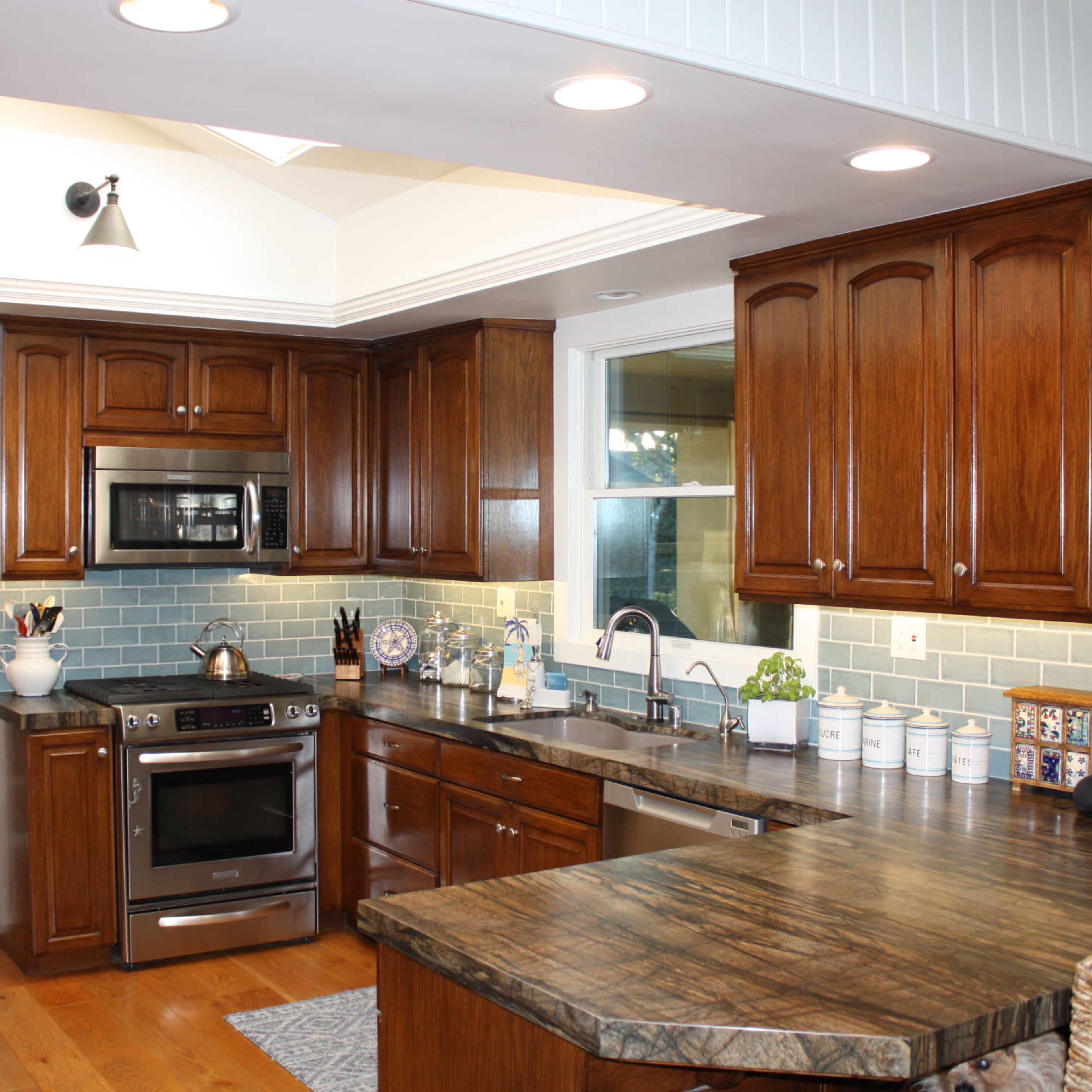 A kitchen with wooden cabinetry, a countertop, stainless steel appliances, and blue-tiled backsplash.
