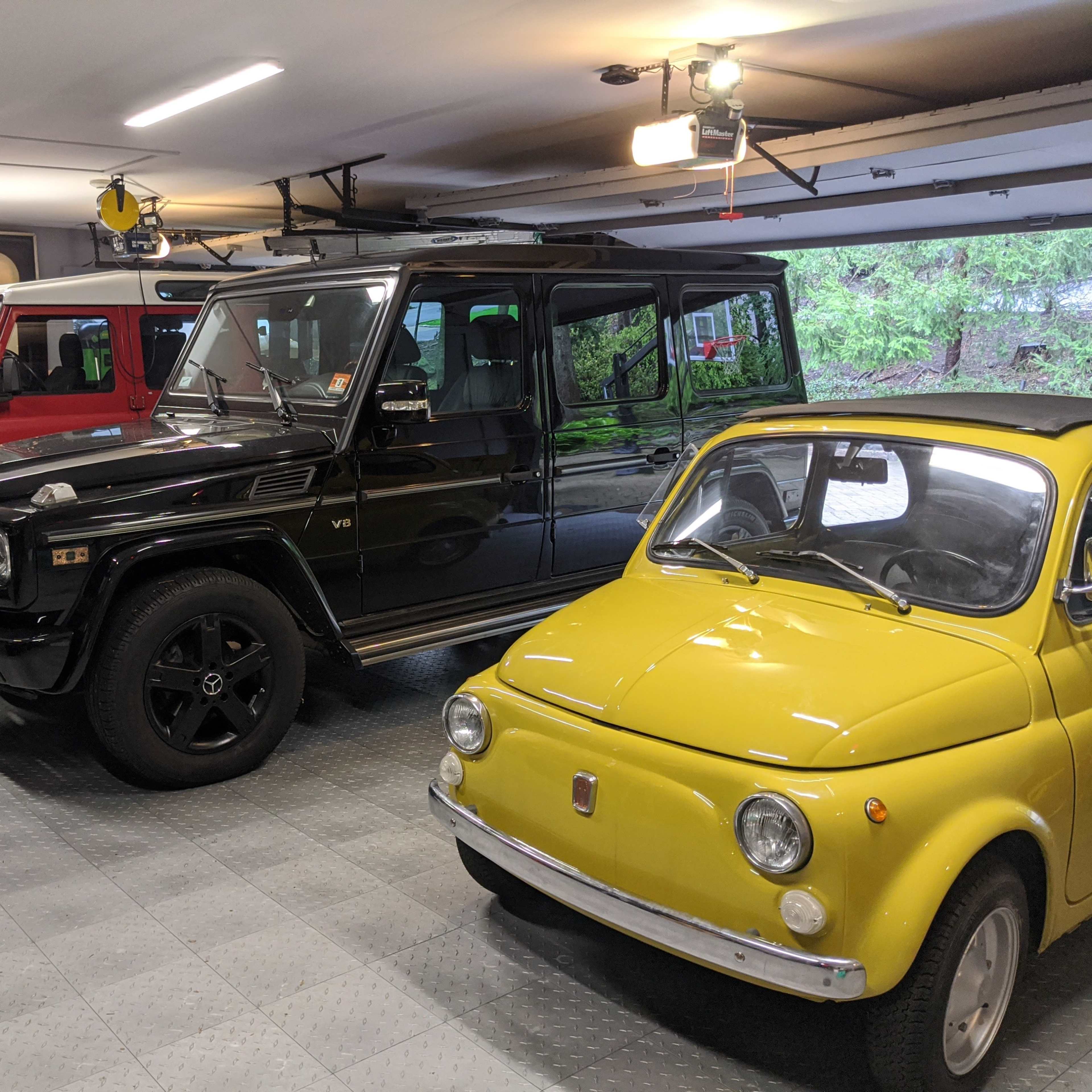 A garage containing three cars: a black SUV, a red utility vehicle, and a yellow compact car.