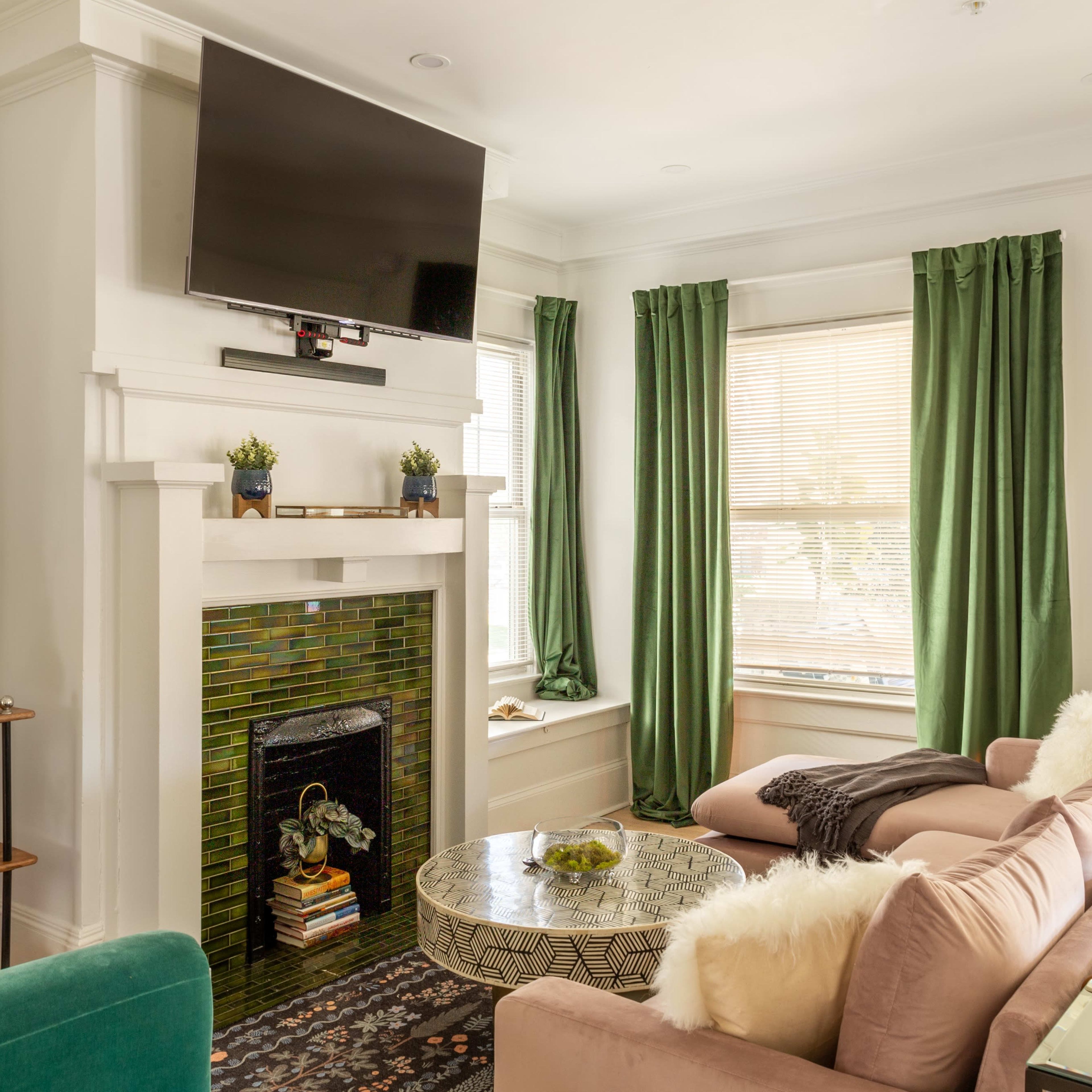 A living room with a green and white color scheme, featuring a flat-screen TV above a fireplace, a coffee table, and a sofa arranged for seating.