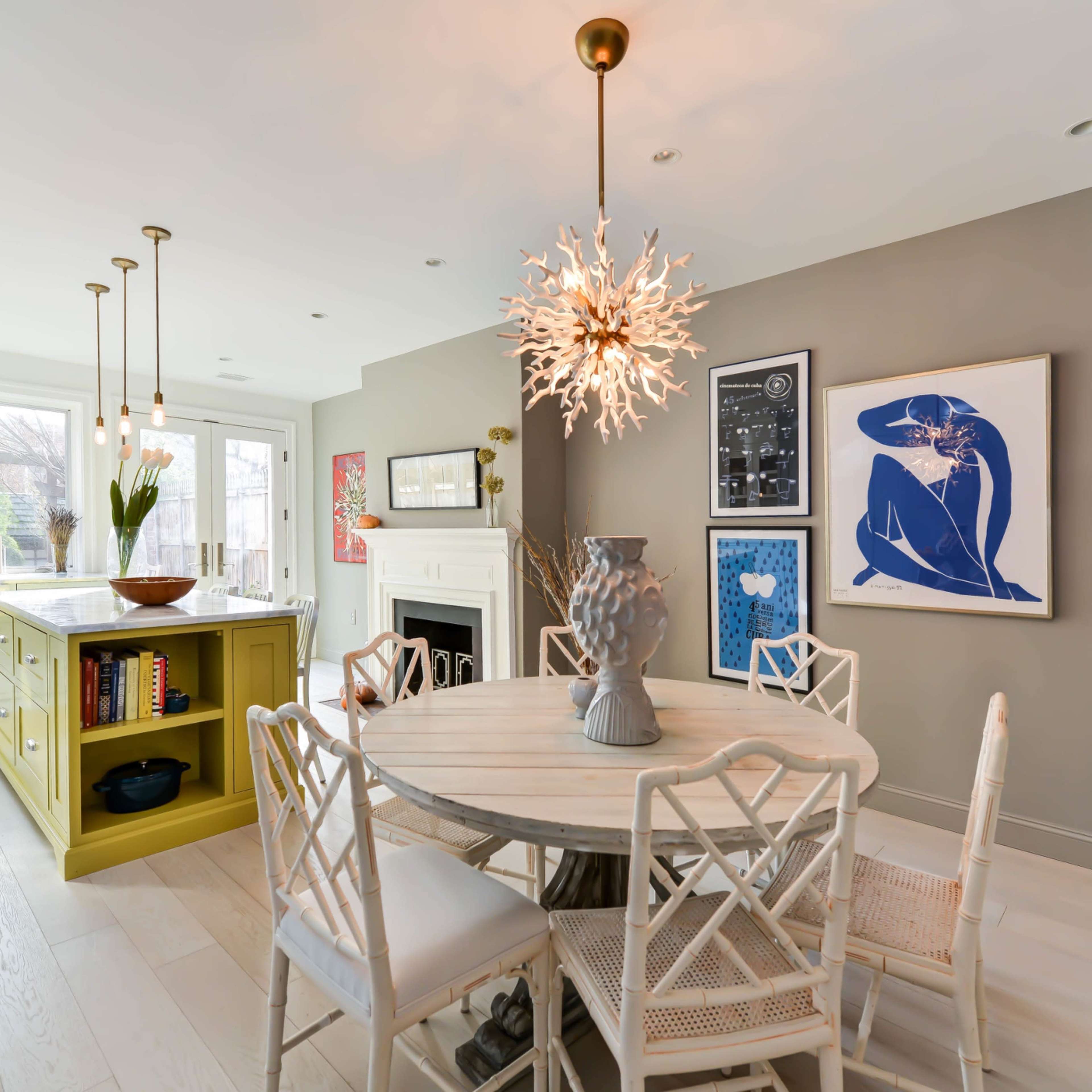 A modern dining area with a round table surrounded by six chairs, a vibrant yellow kitchen island, and a large window allowing natural light to illuminate the space.