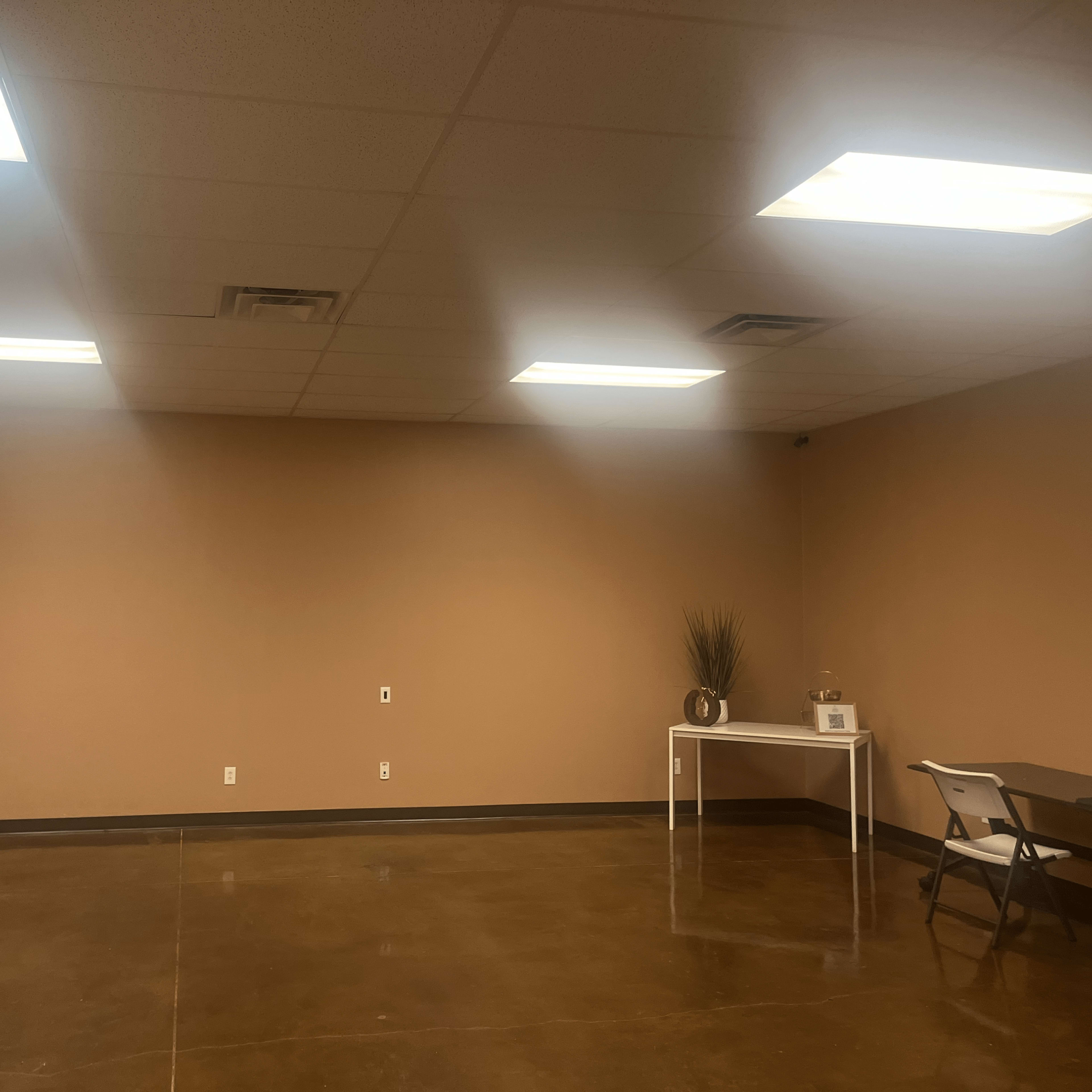 An empty room with a polished concrete floor, light brown walls, and overhead fluorescent lighting.