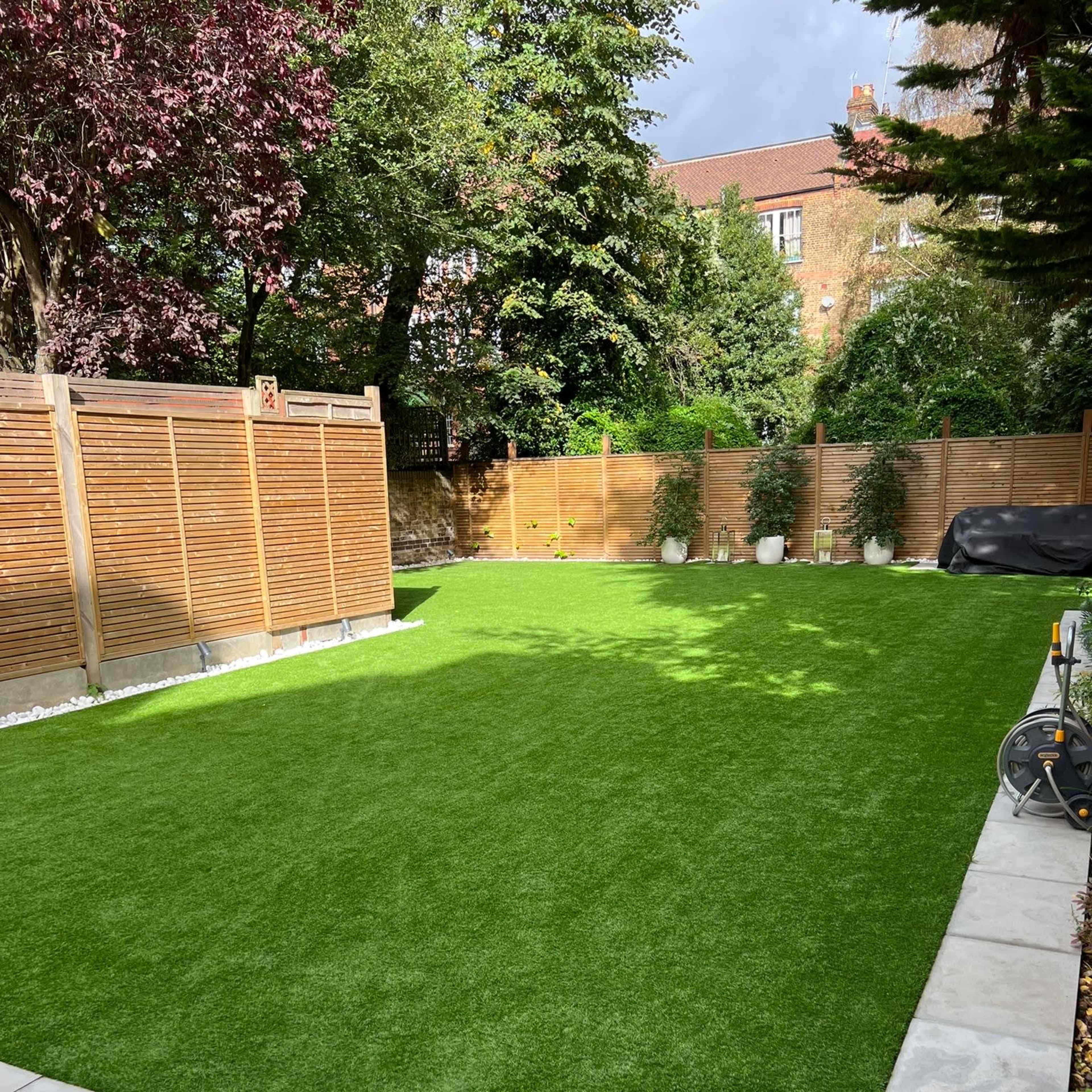A neatly maintained lawn with artificial grass surrounded by wooden fences and a paved area.