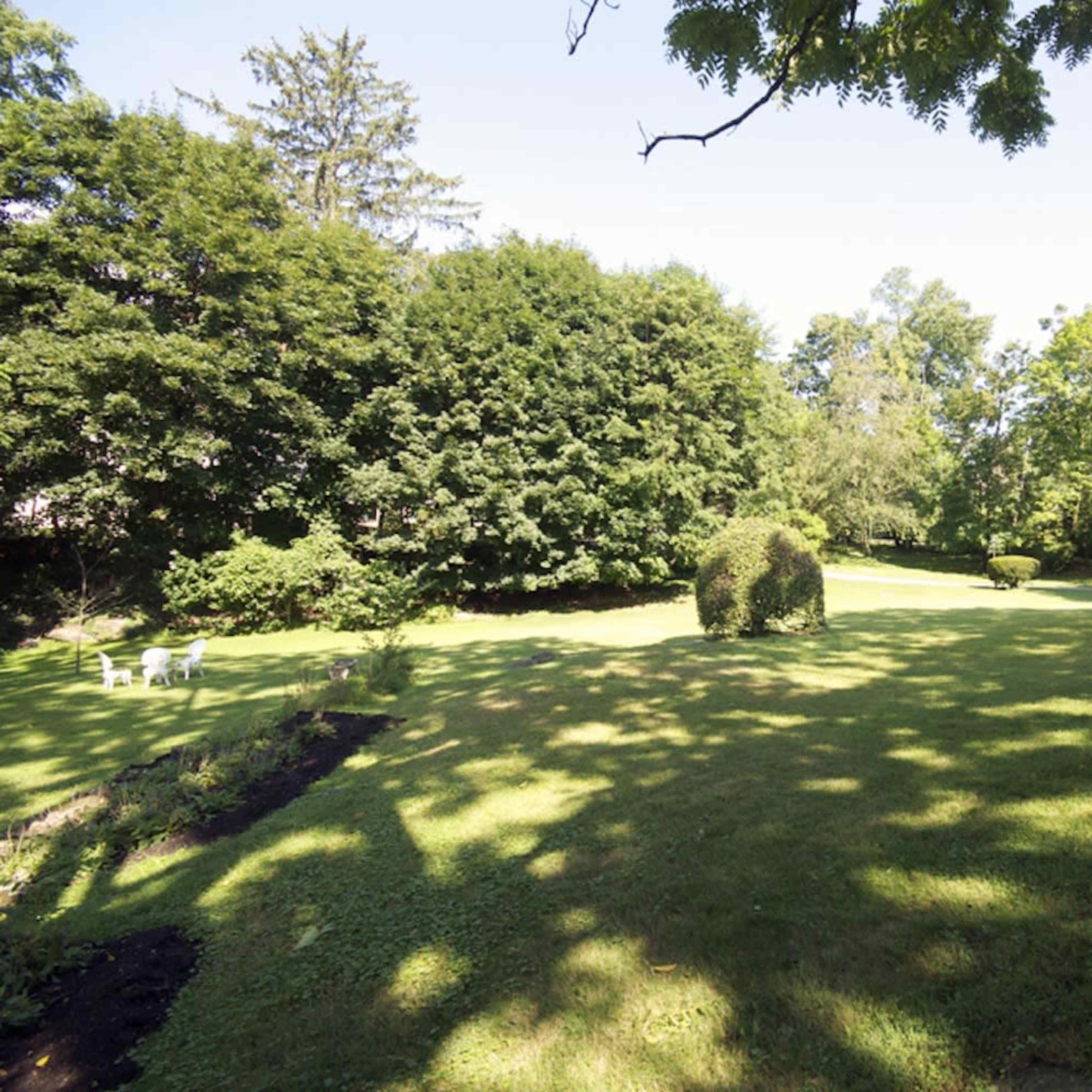 A spacious green lawn bordered by trees and a few garden chairs in the background.