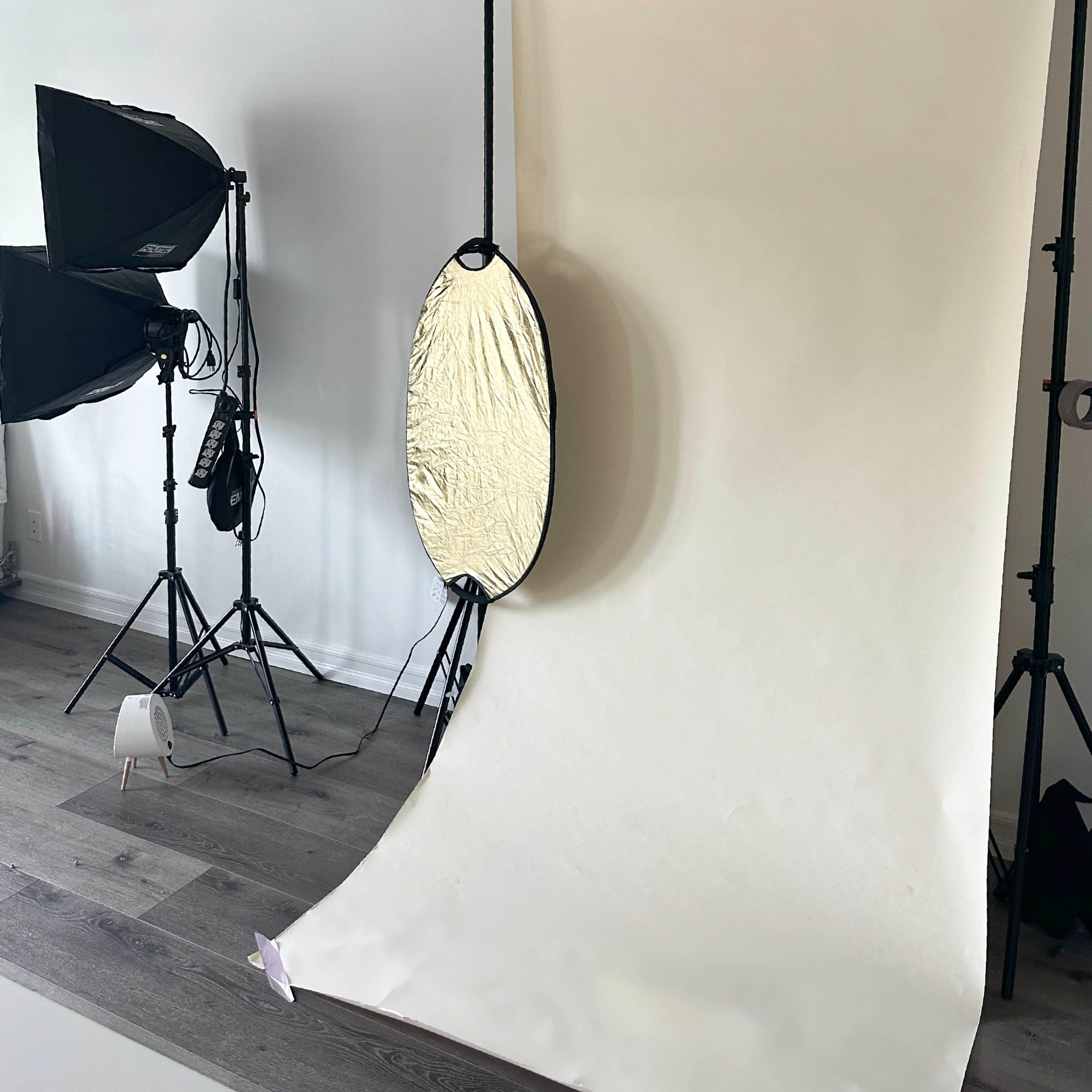 A photography studio setup with a white backdrop, softbox lights, and a reflector on stands.