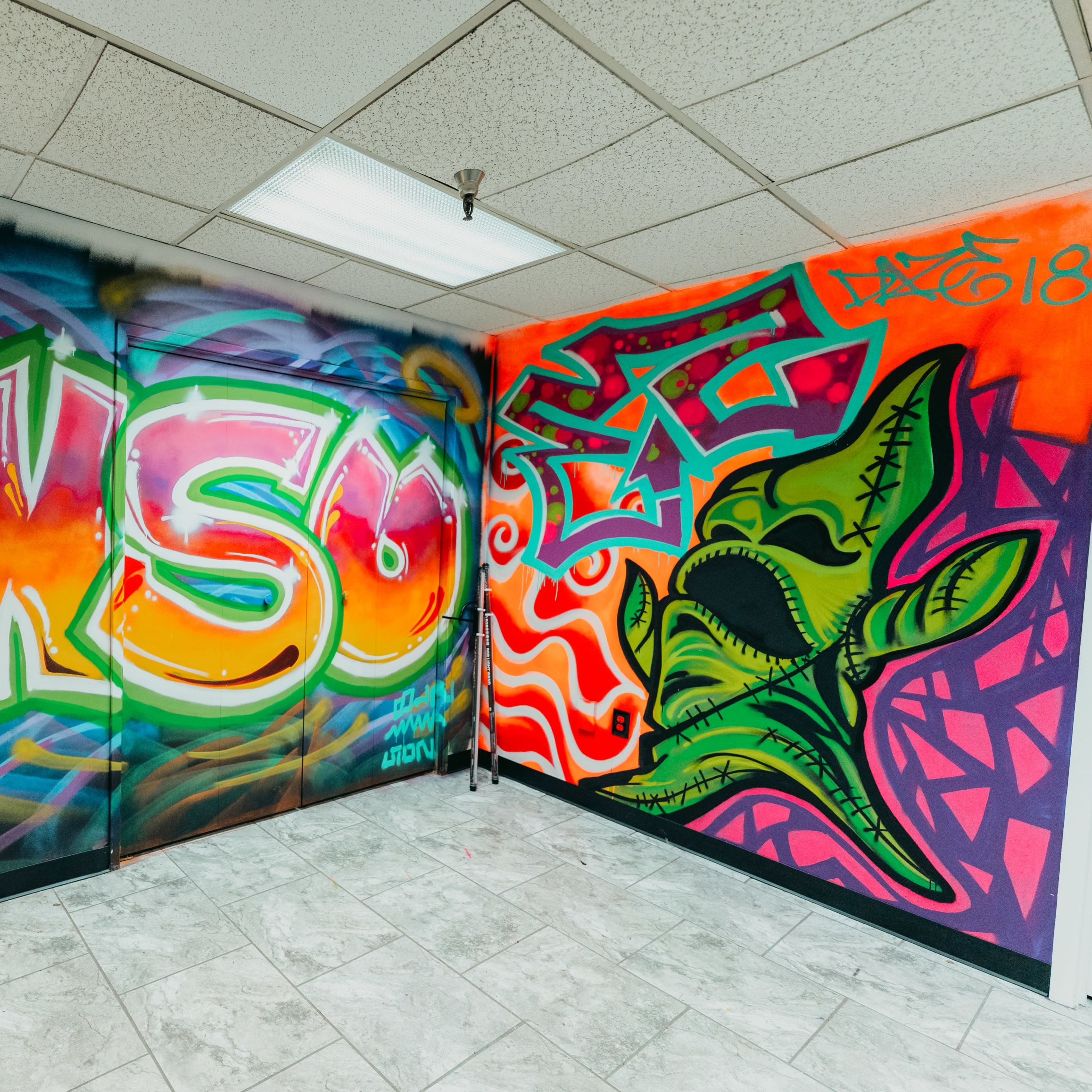 A room corner with vibrant graffiti art covering two walls, featuring colorful lettering and a green cartoonish creature.