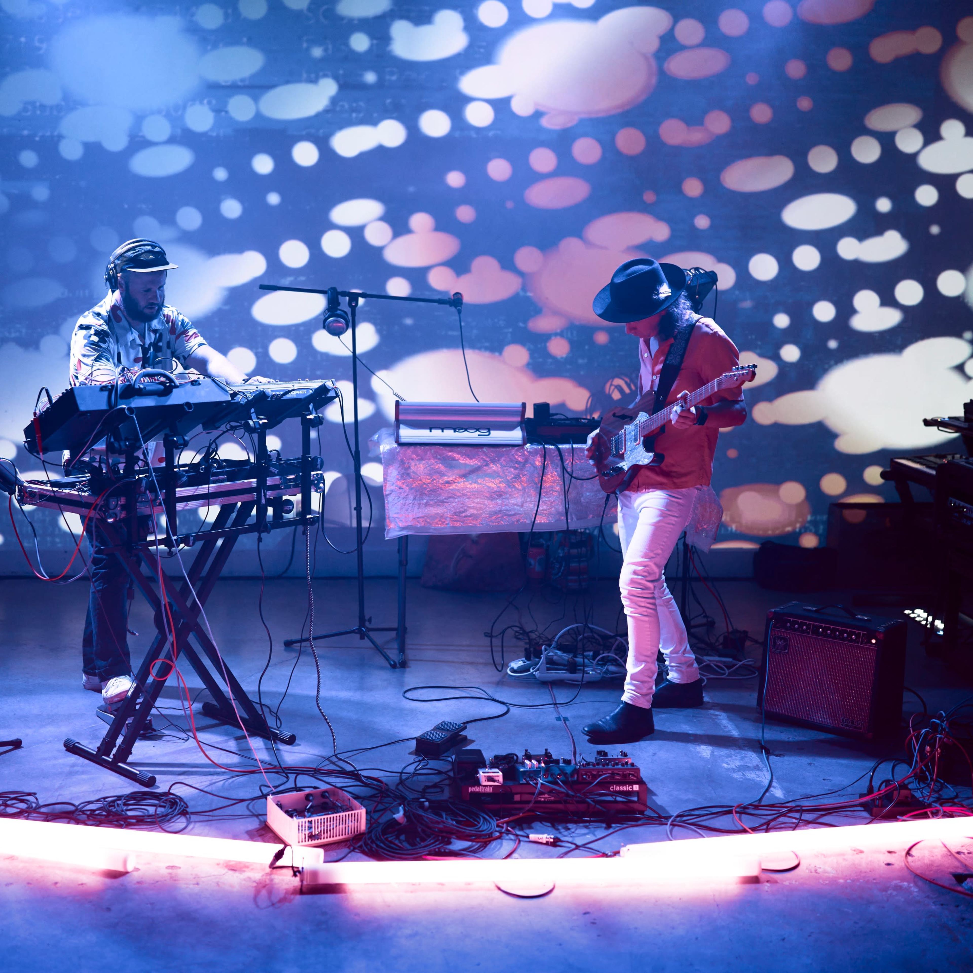 A dancer performs on a stage illuminated by colorful lights in an industrial space.