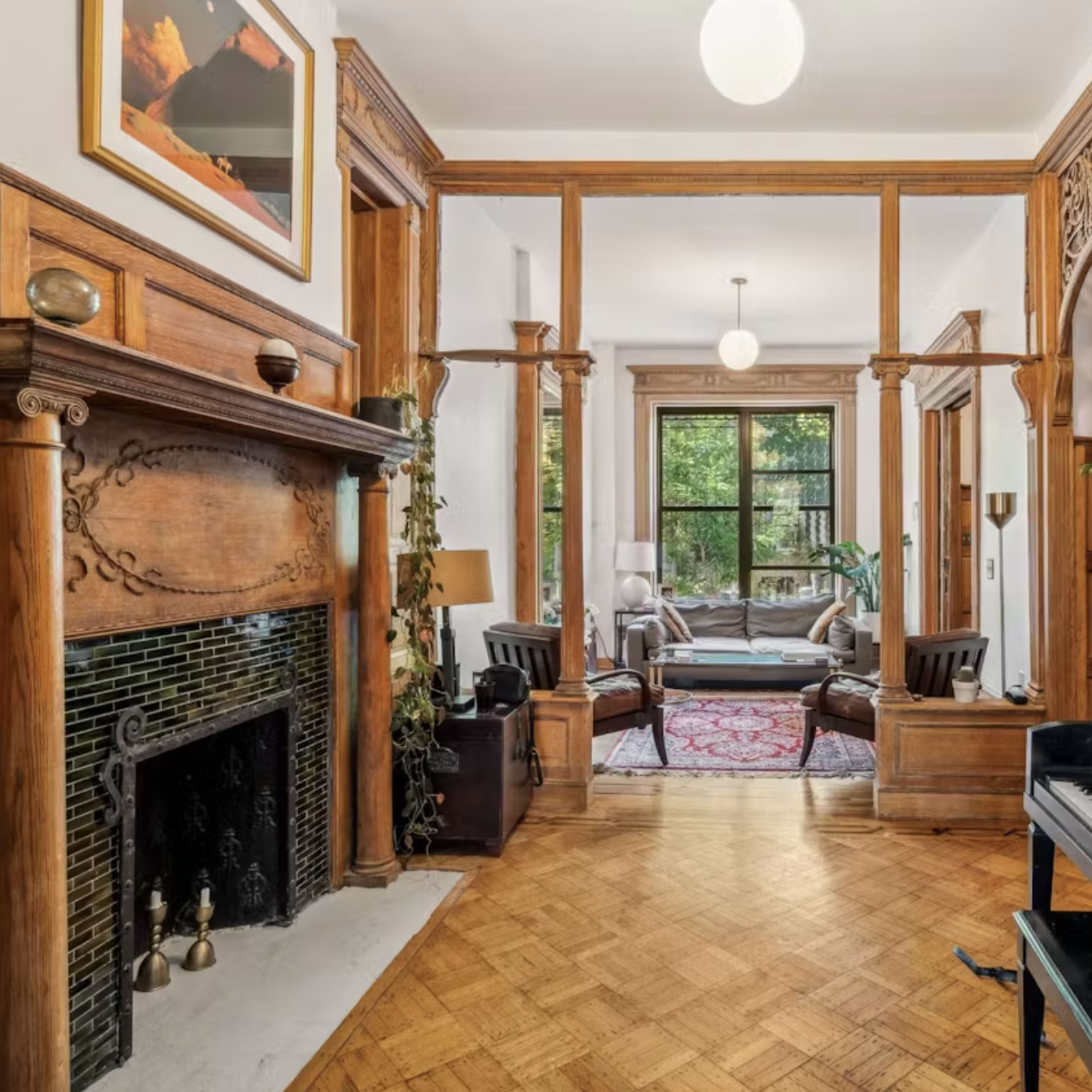 A spacious foyer with a wooden fireplace, a piano in the foreground, and a view of a living area through arched doorways.