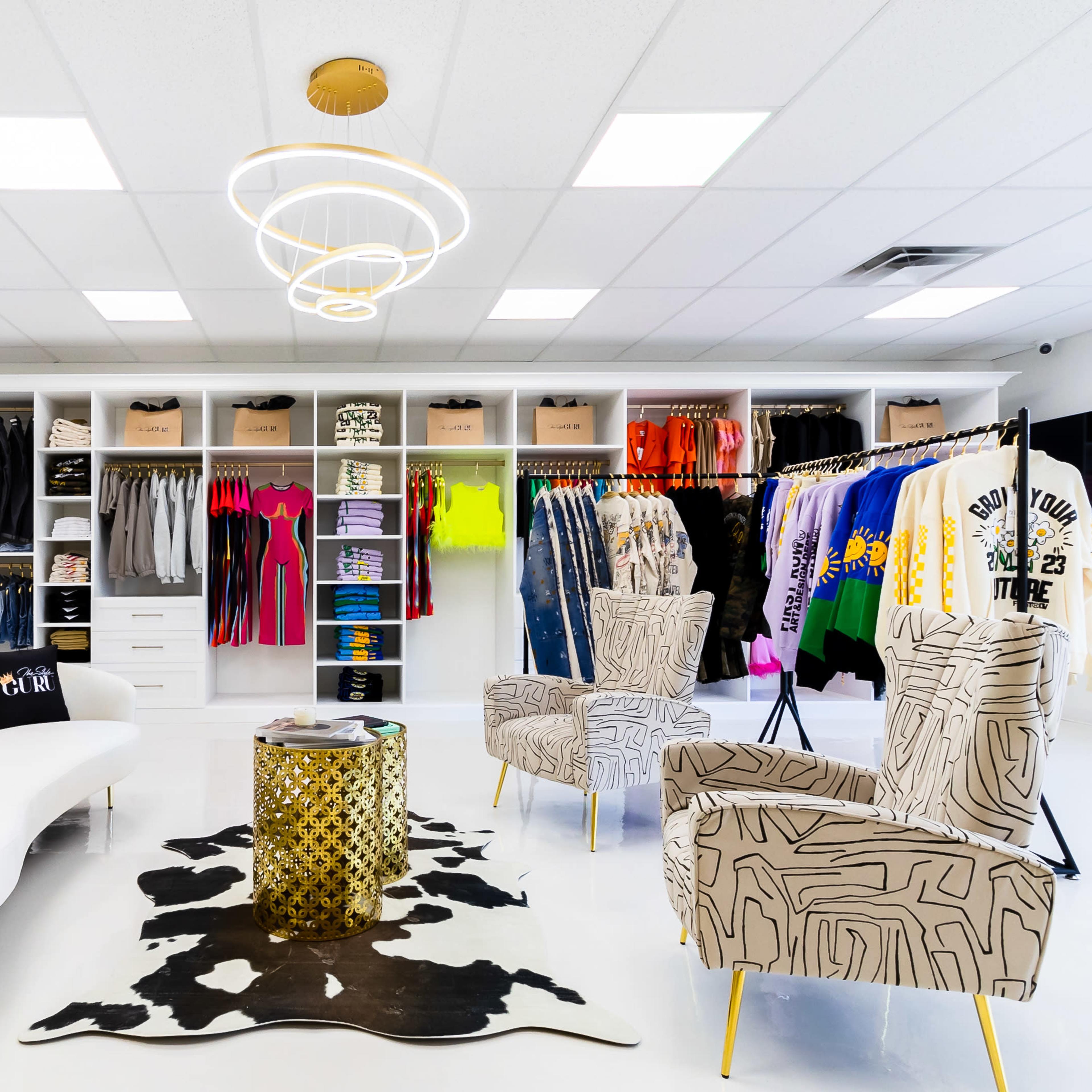 A clothing boutique with neatly organized racks of colorful apparel and stylish seating arrangements in a bright, modern interior.