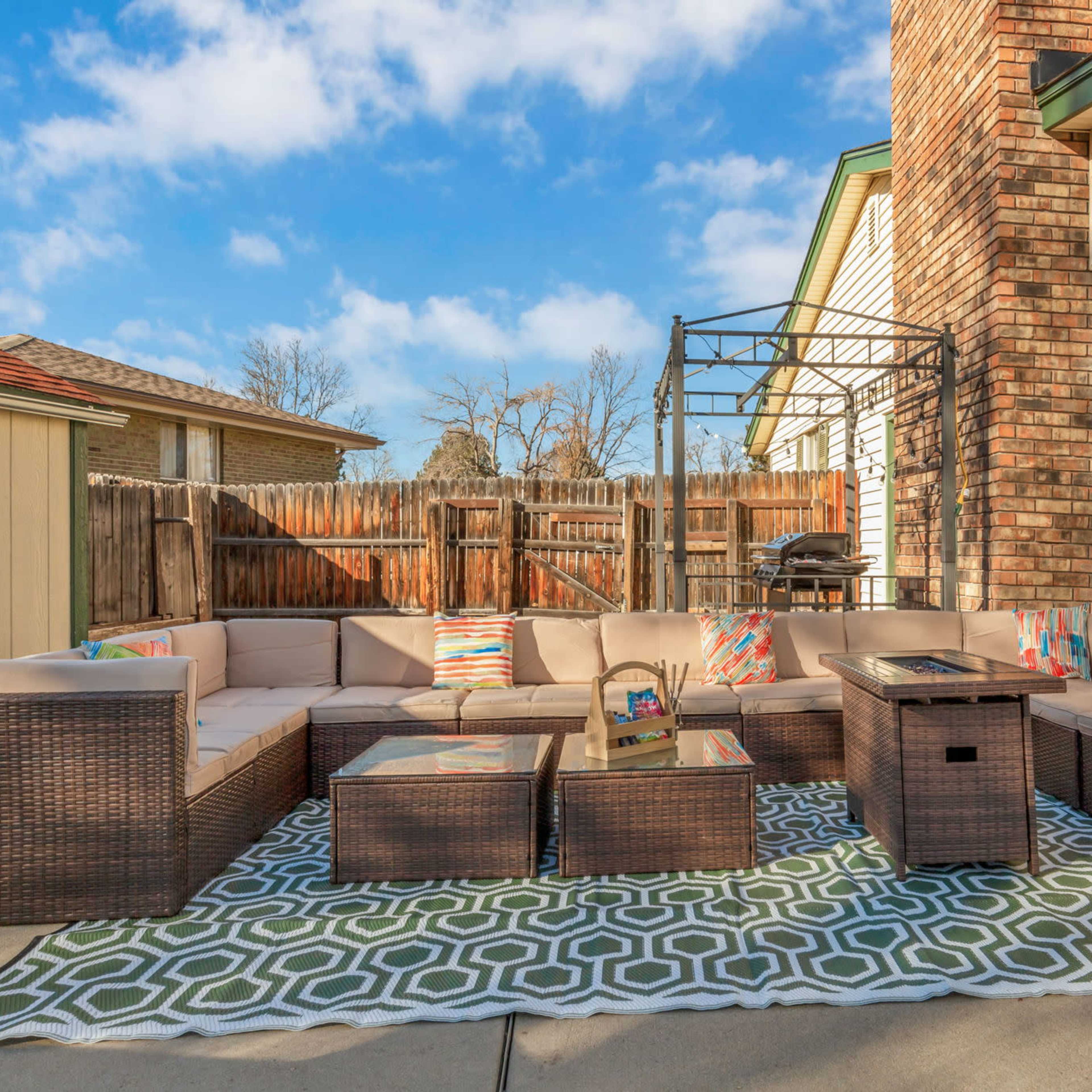 A patio area features a large sectional sofa, several coffee tables, and a gazebo, set against a backdrop of a wooden fence and houses.