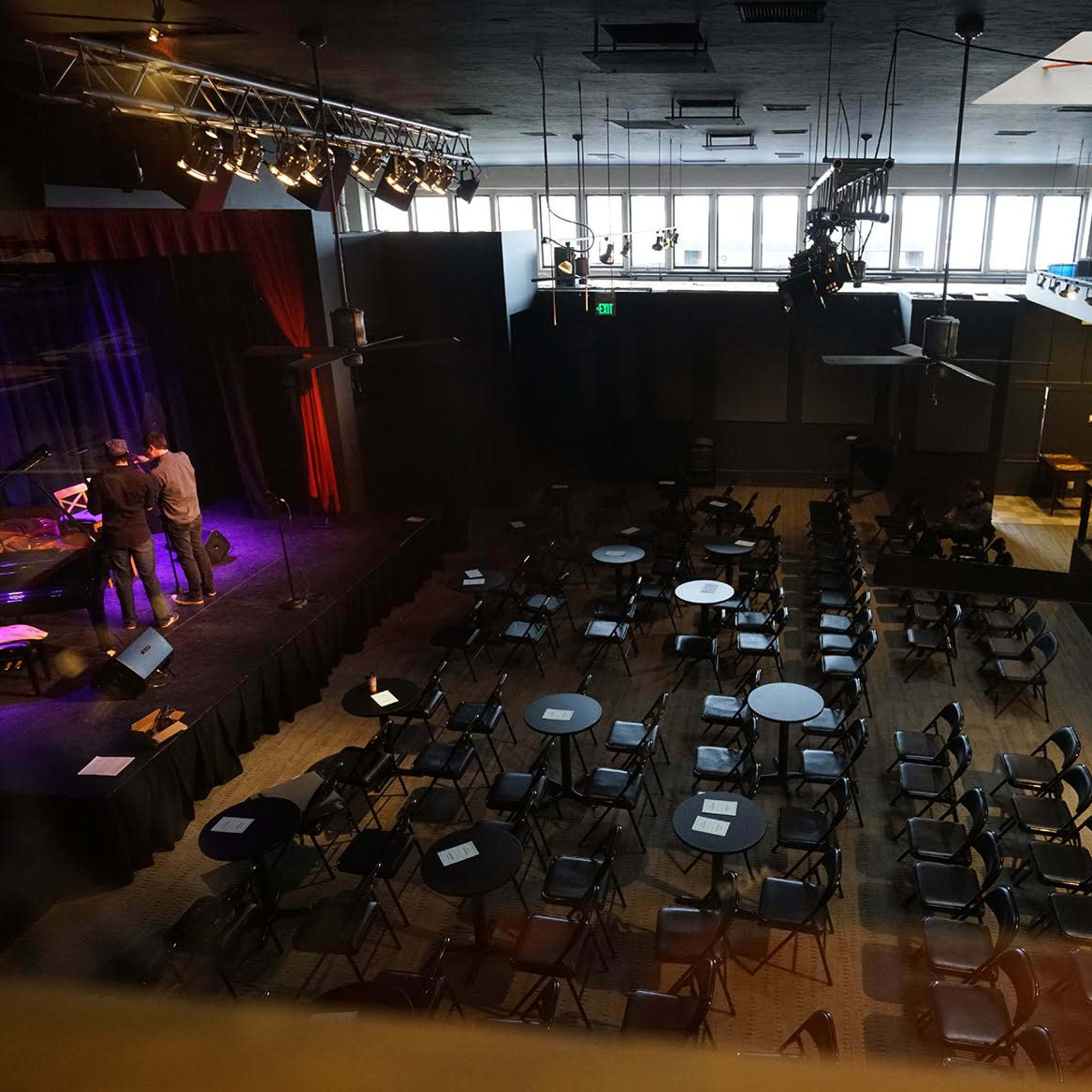 A performance venue with a raised stage and rows of empty chairs and tables arranged in front of it.