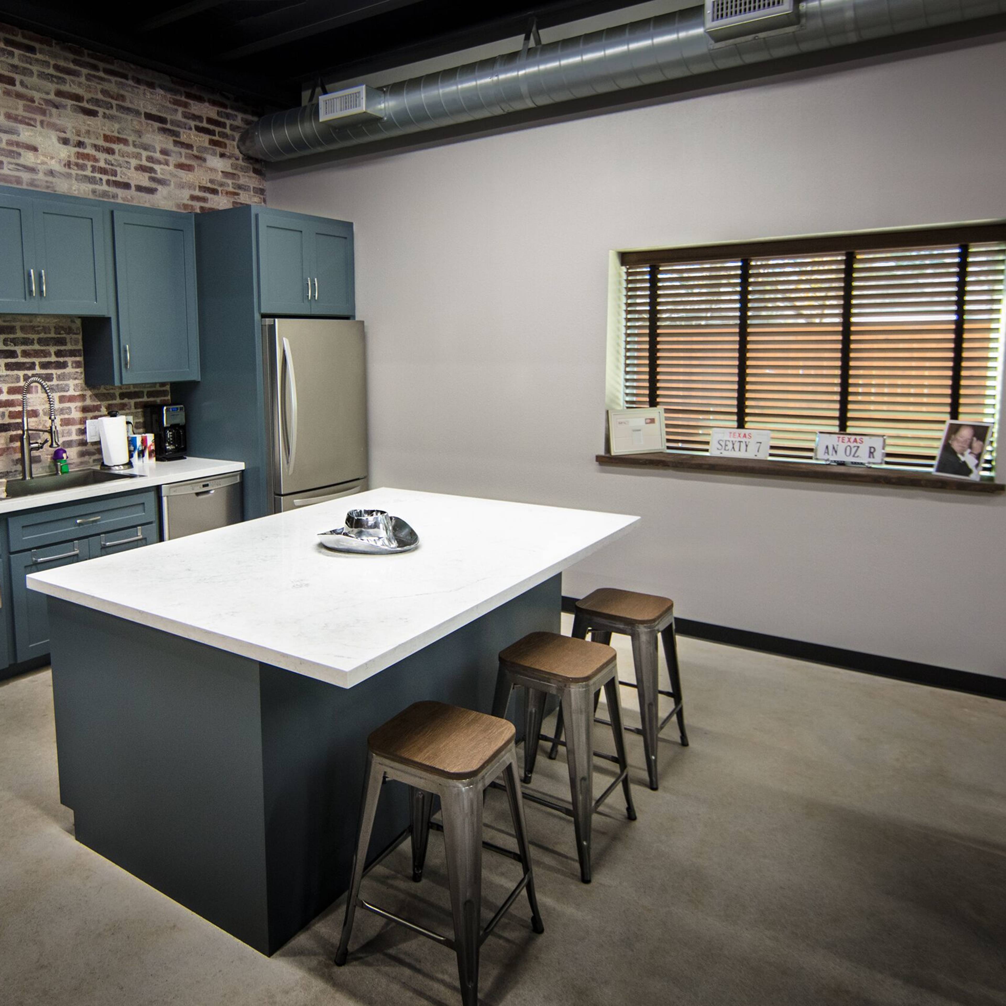 A modern kitchen featuring blue cabinetry, stainless steel appliances, and a white marble island with three wooden stools.