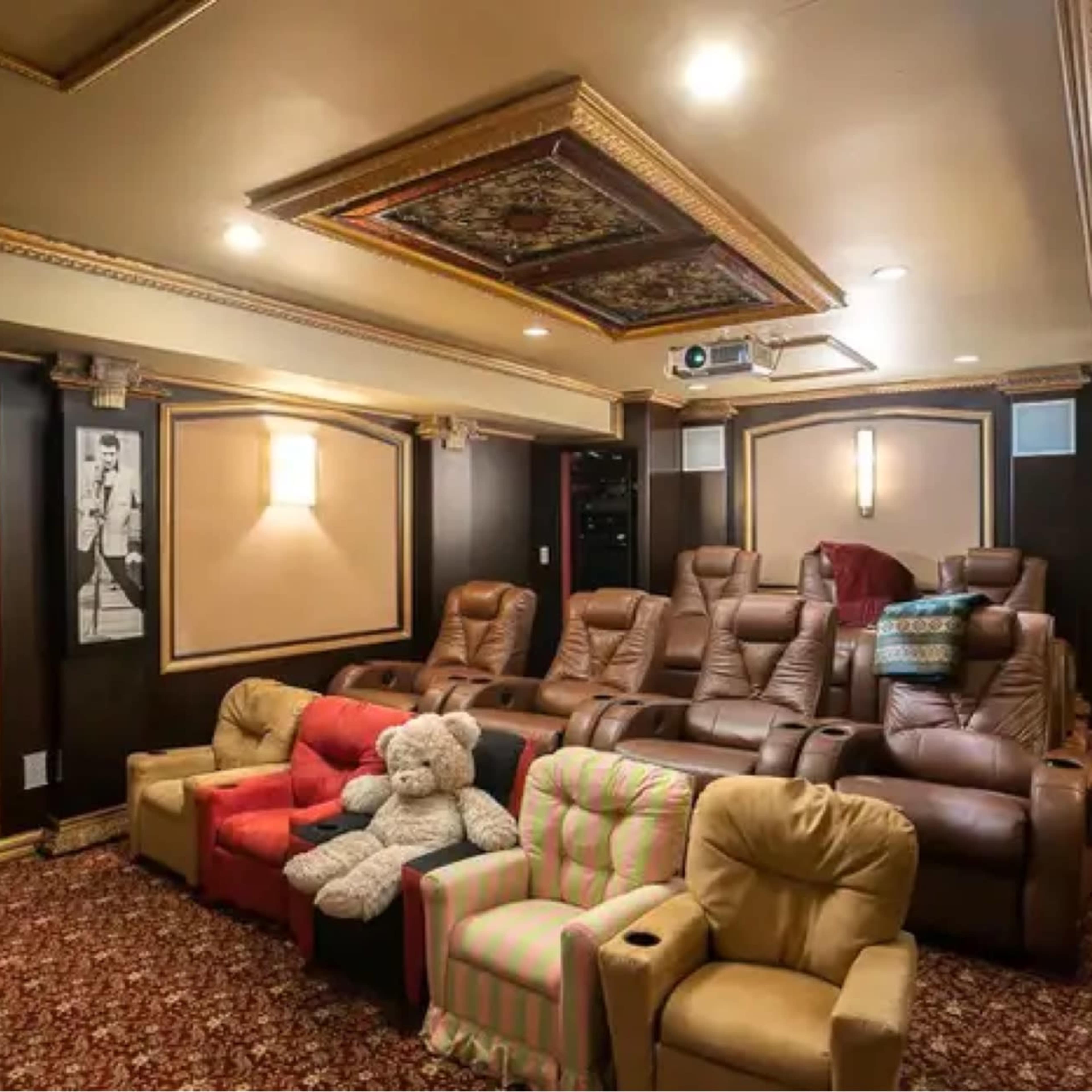 A home theater room with plush reclining chairs arranged in a semicircle, featuring a projector and decorative ceiling details.