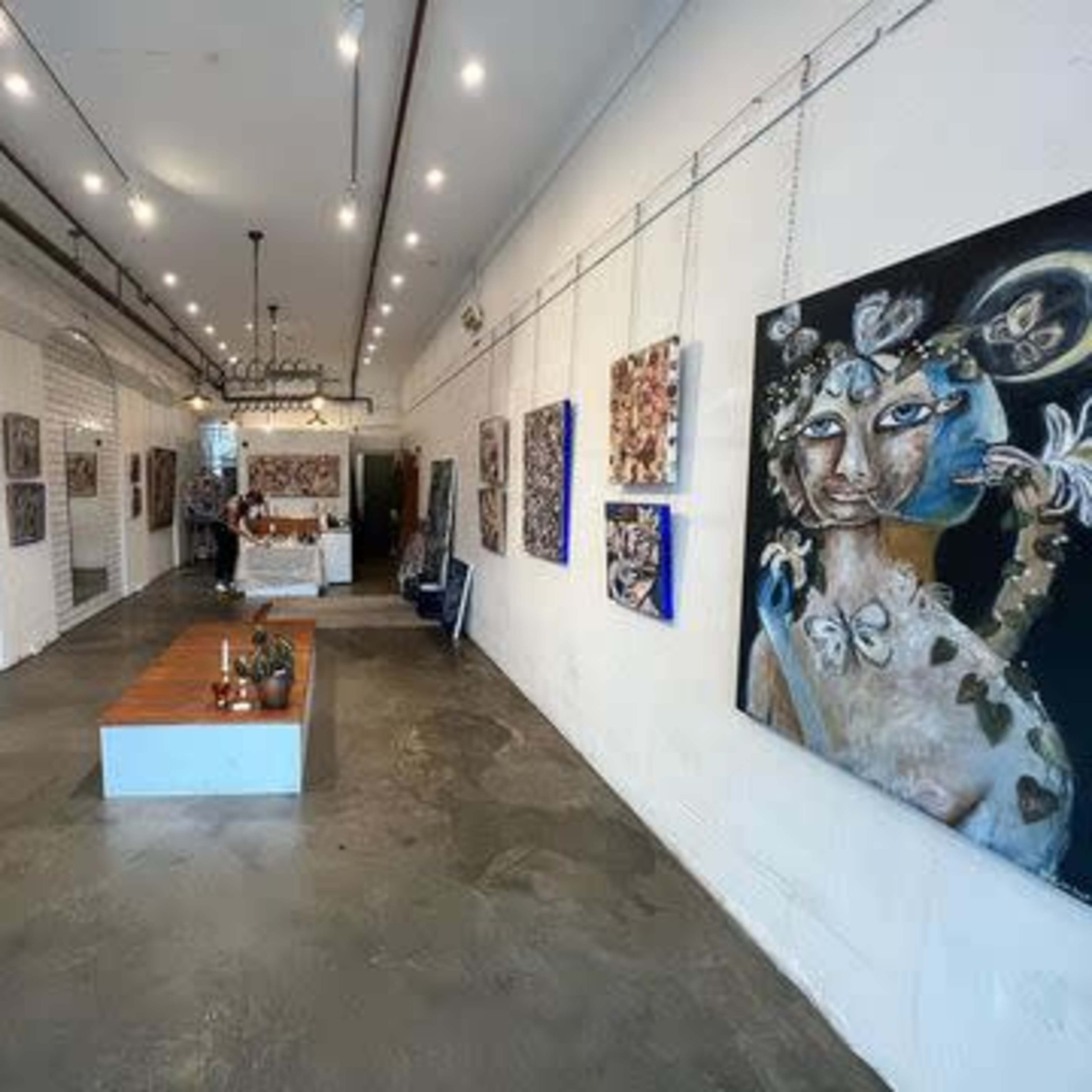 A modern art gallery with paintings displayed on the white walls and a wooden table in the center of the space.