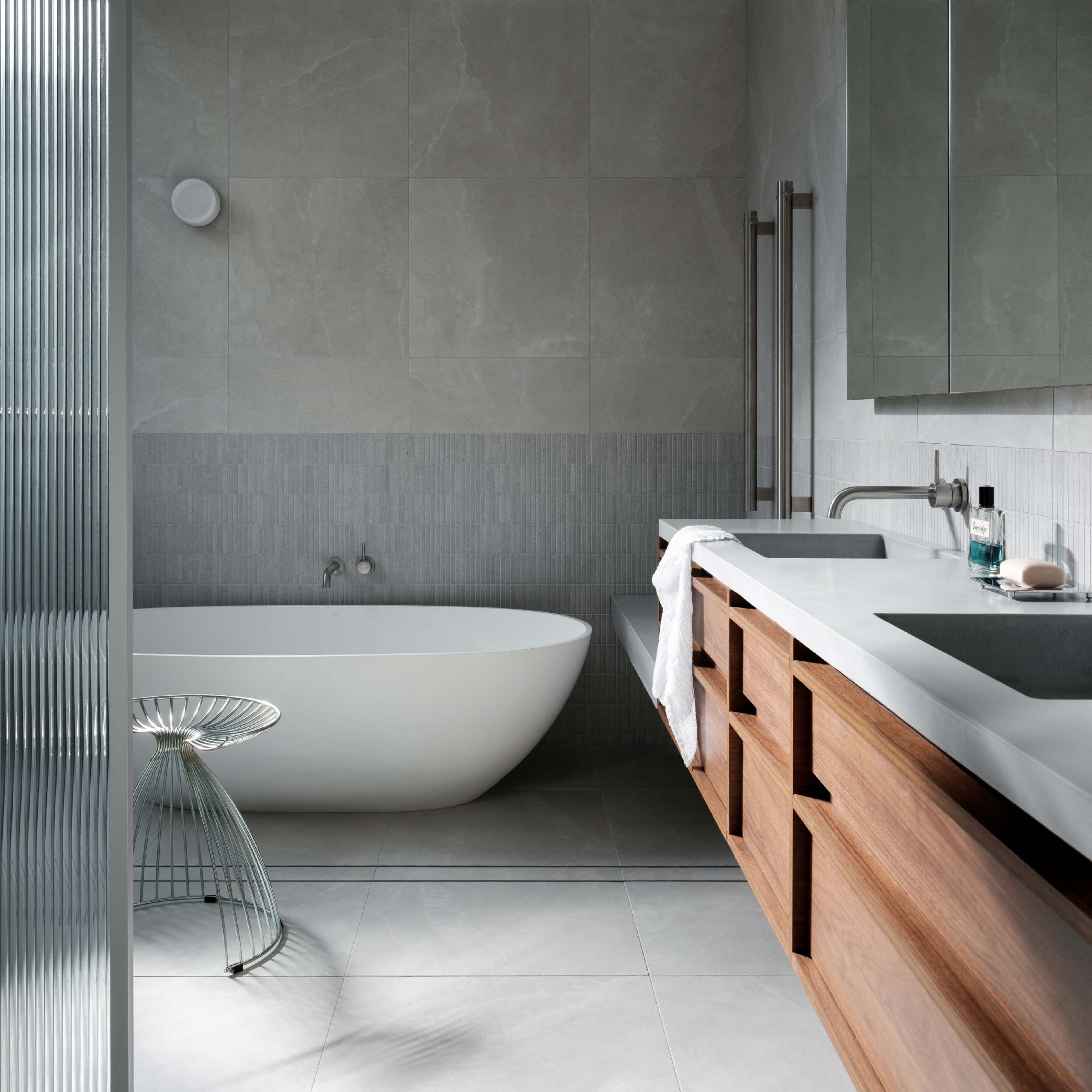 A modern bathroom featuring a freestanding white bathtub, a wooden vanity with multiple drawers, and a large mirror reflecting the uncluttered space.