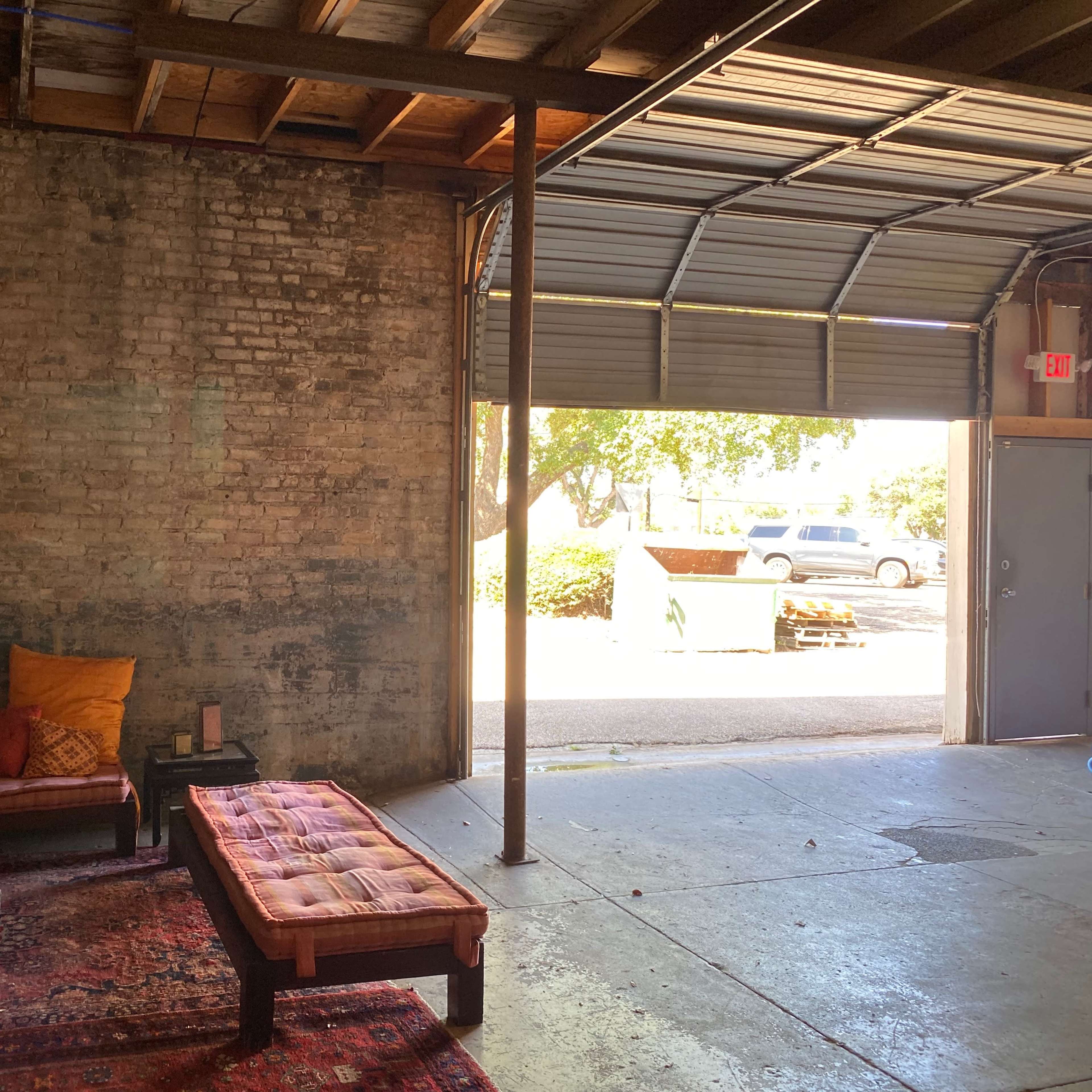 An open garage features a seating area with colorful cushions and a view of a driveway outside.