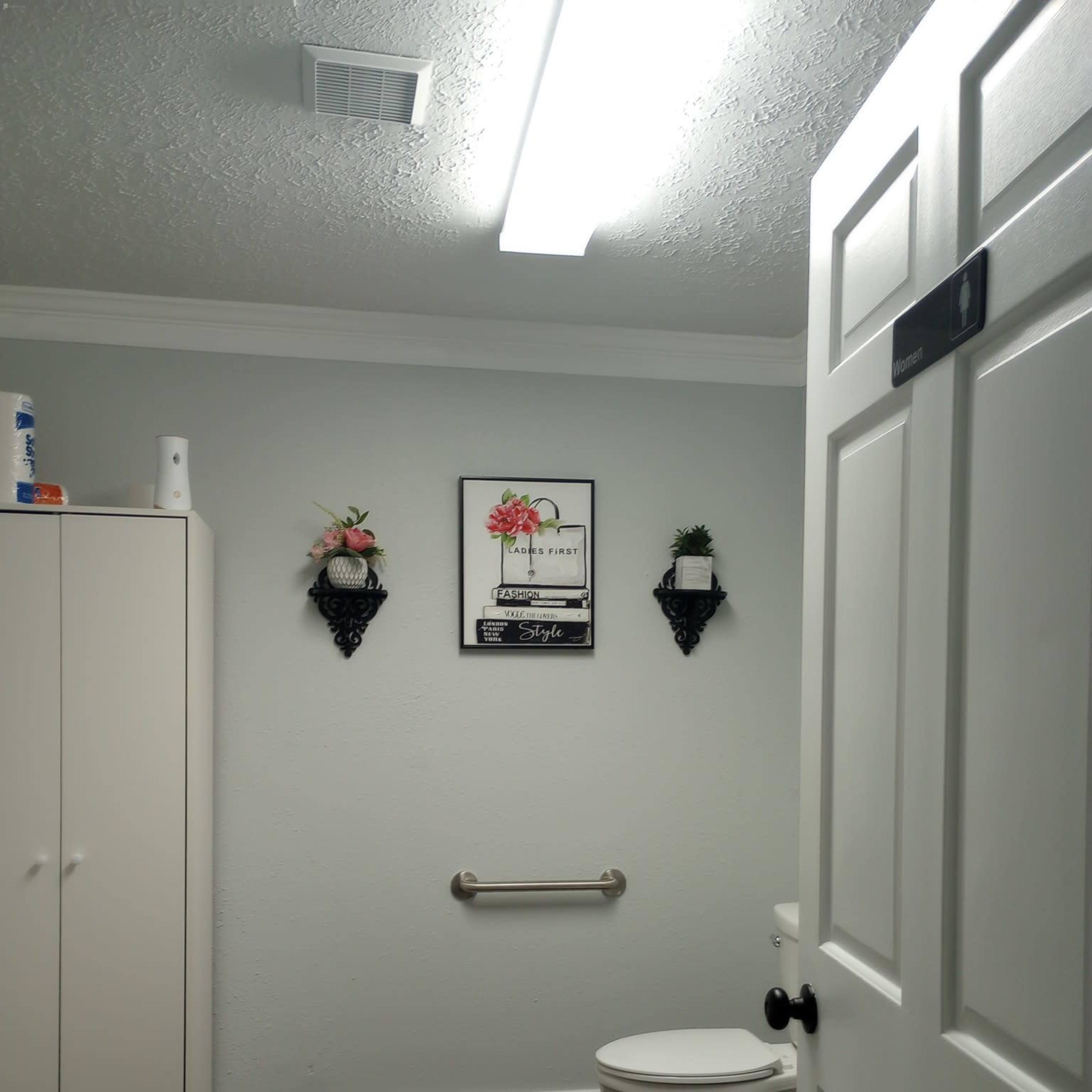 A bathroom with a toilet, white cabinetry, a towel rack, and decorative wall elements.