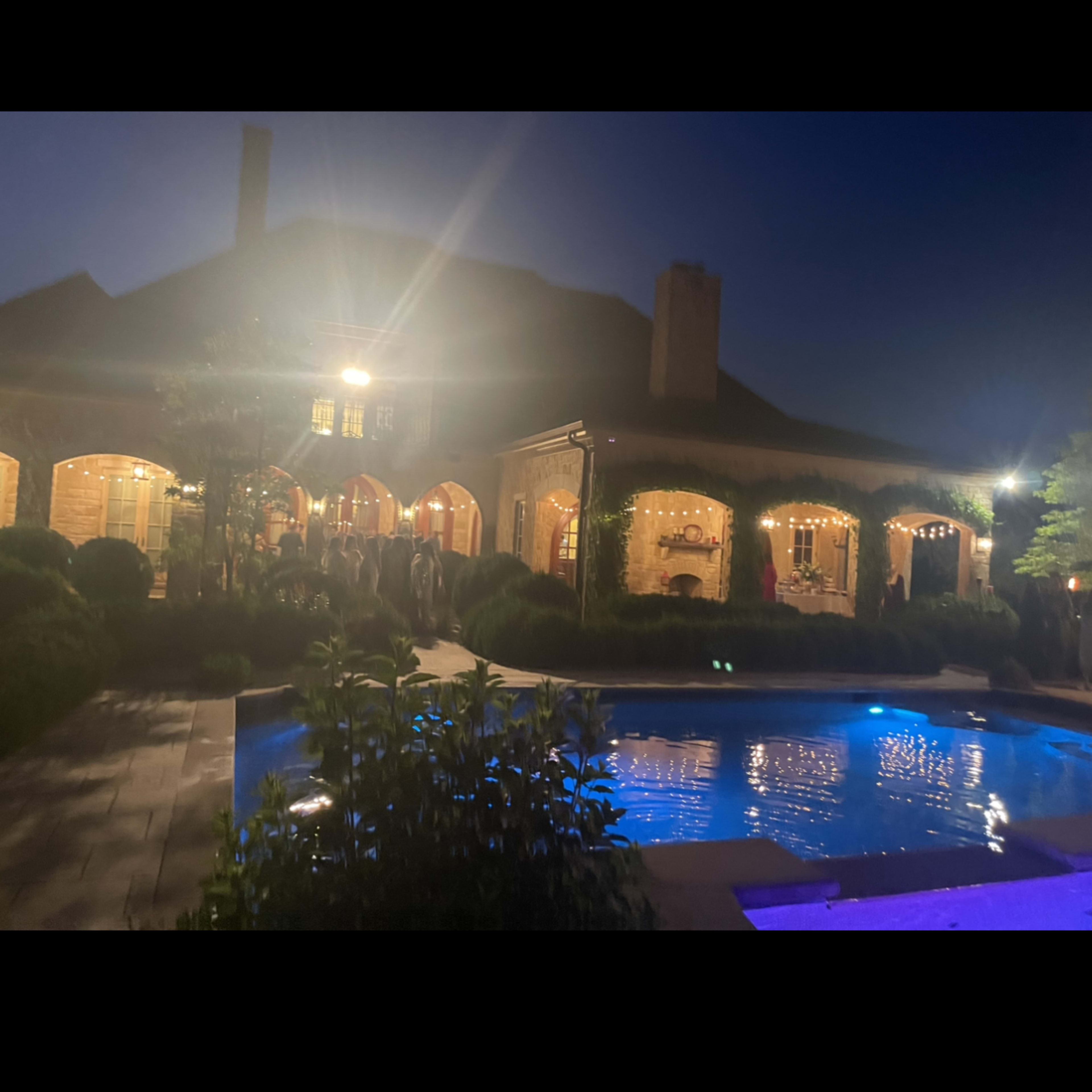 A well-lit house with outdoor features overlooks a swimming pool during twilight.