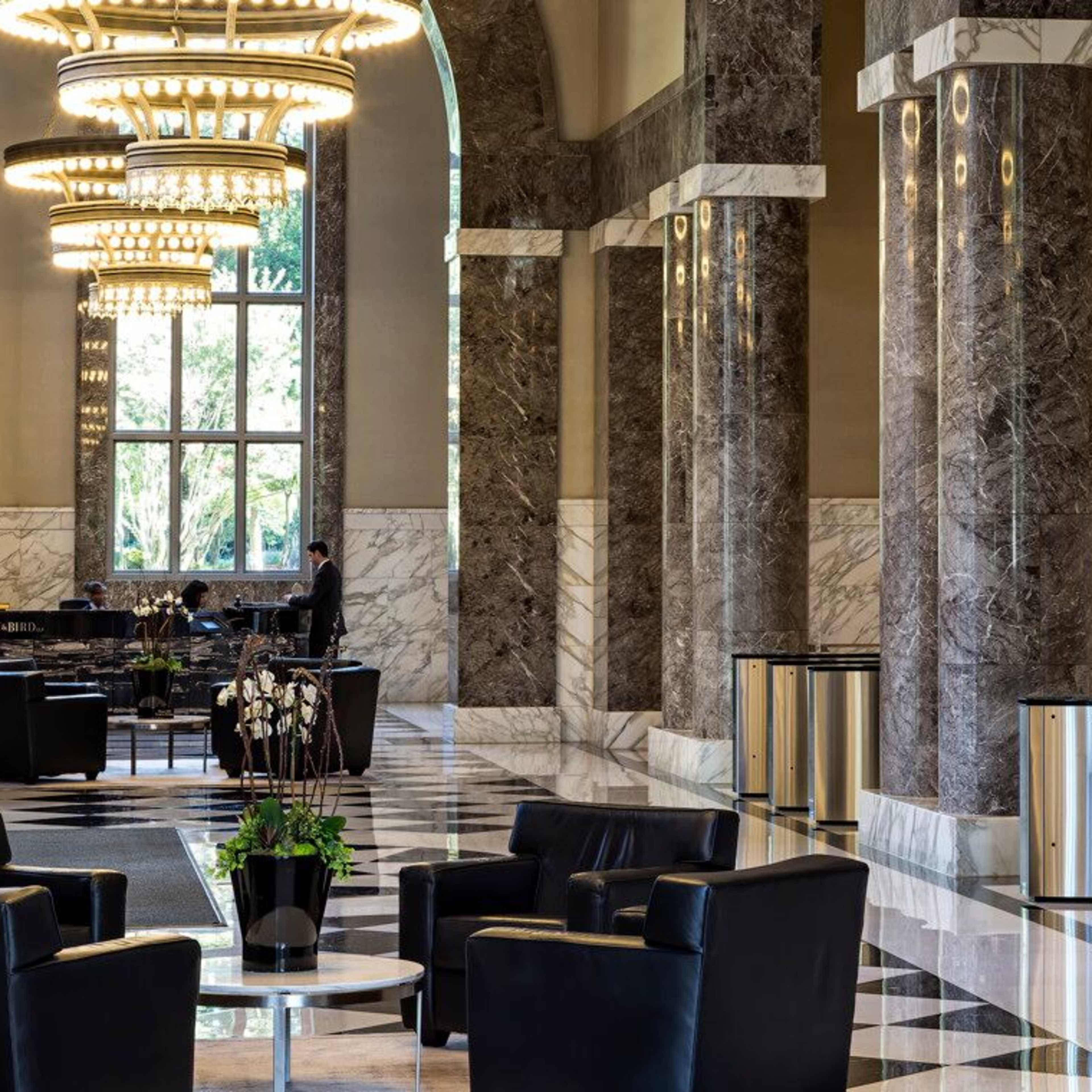 A spacious lobby with marble columns, large windows, and modern seating arranged around a circular coffee table.