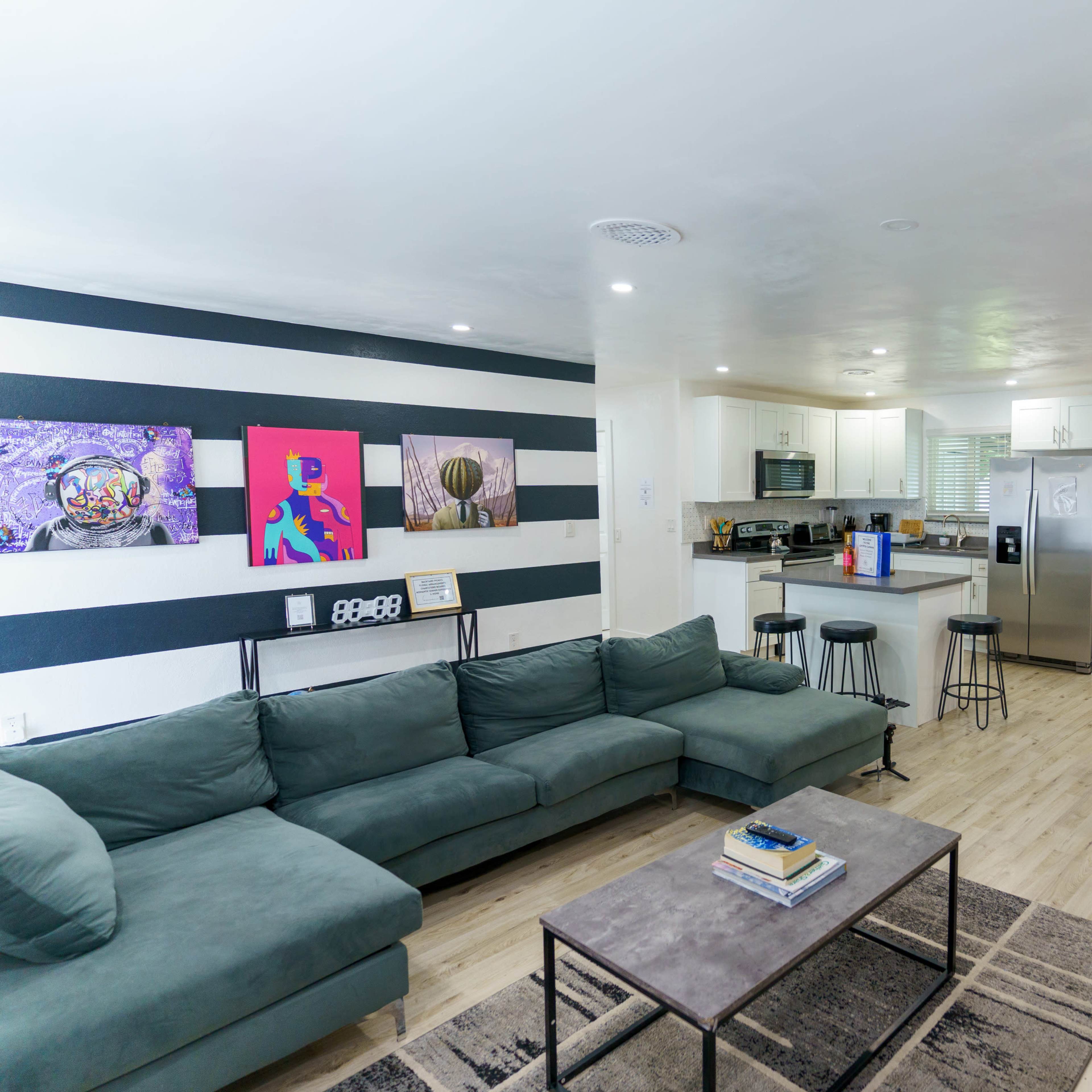 A modern open-concept living area features a sectional sofa, a coffee table, and a dining table, with a kitchen visible in the background.