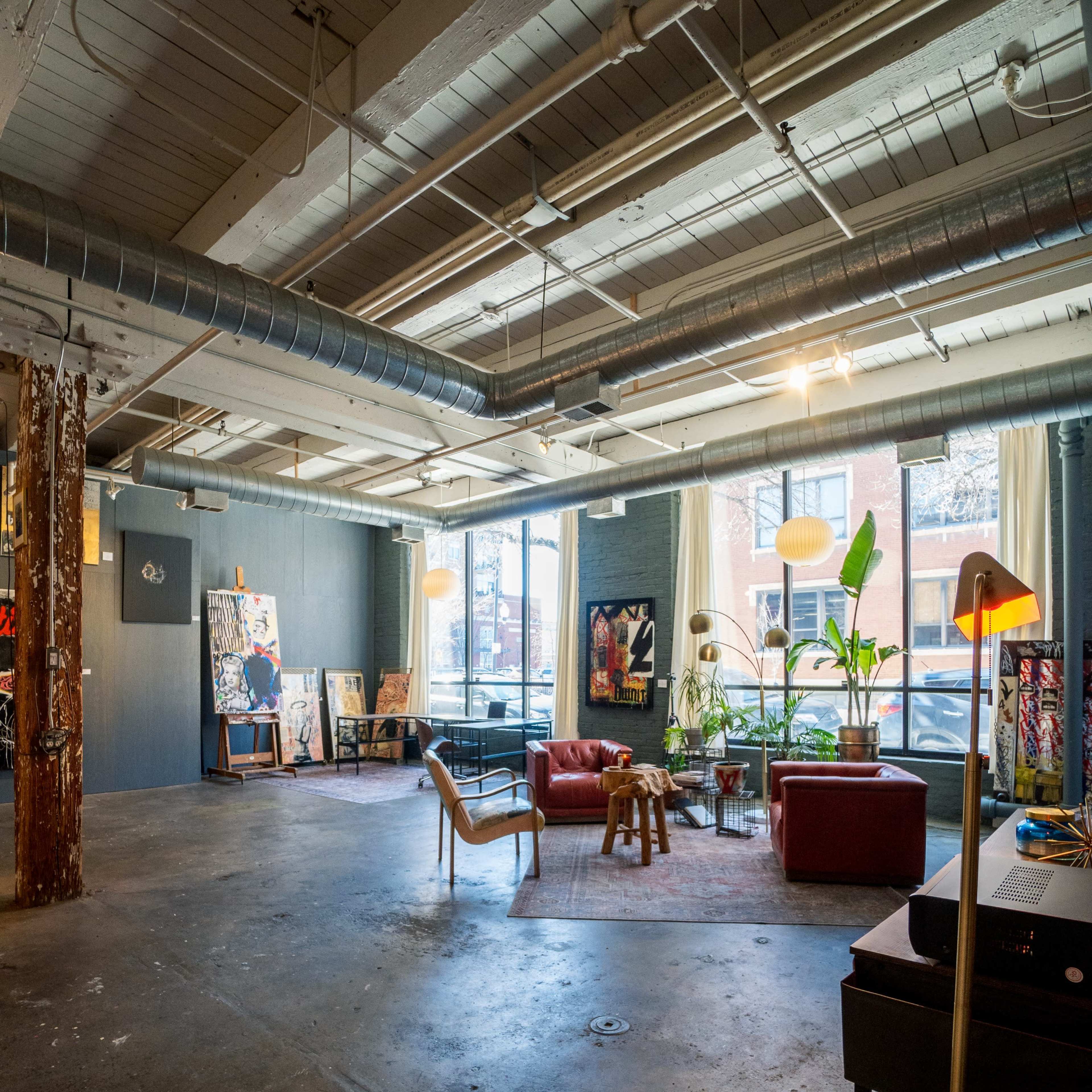 A spacious art studio featuring a red couch, various artworks on the walls, and natural light streaming through large windows.