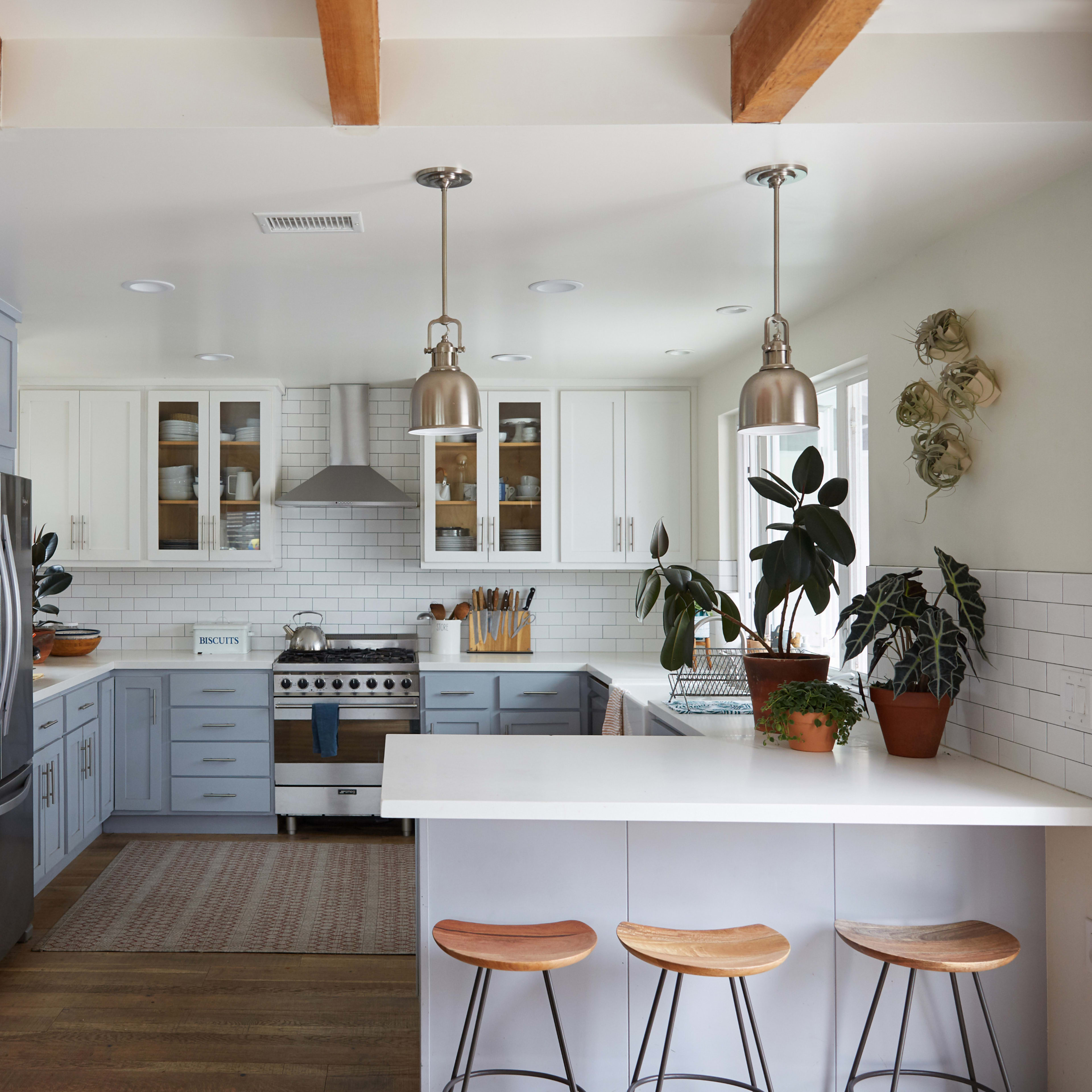 A modern kitchen featuring light blue cabinetry, stainless steel appliances, and a white countertop with bar stools.