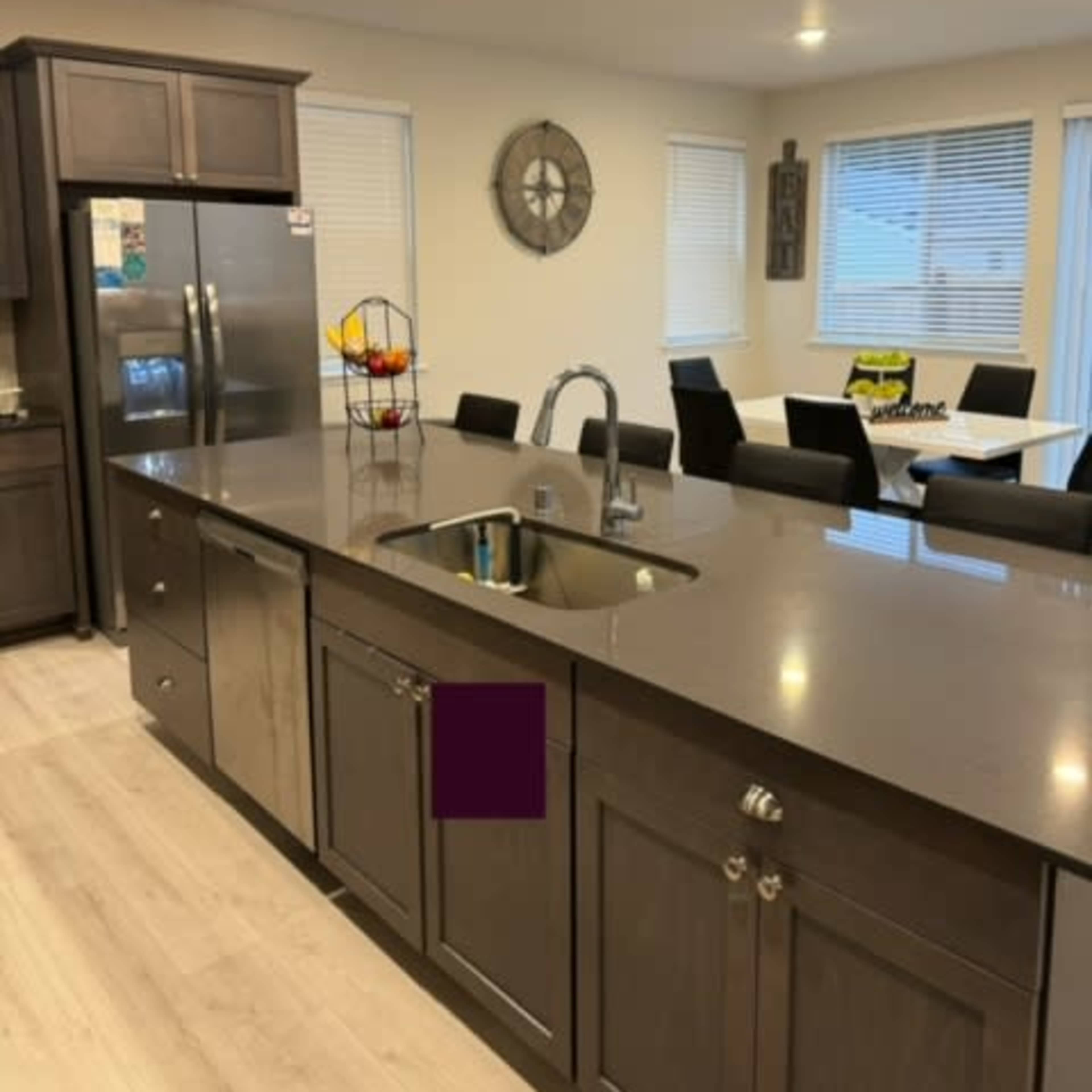 A modern kitchen with dark wooden cabinetry, a stainless steel refrigerator, and a dining area featuring a table and black chairs.