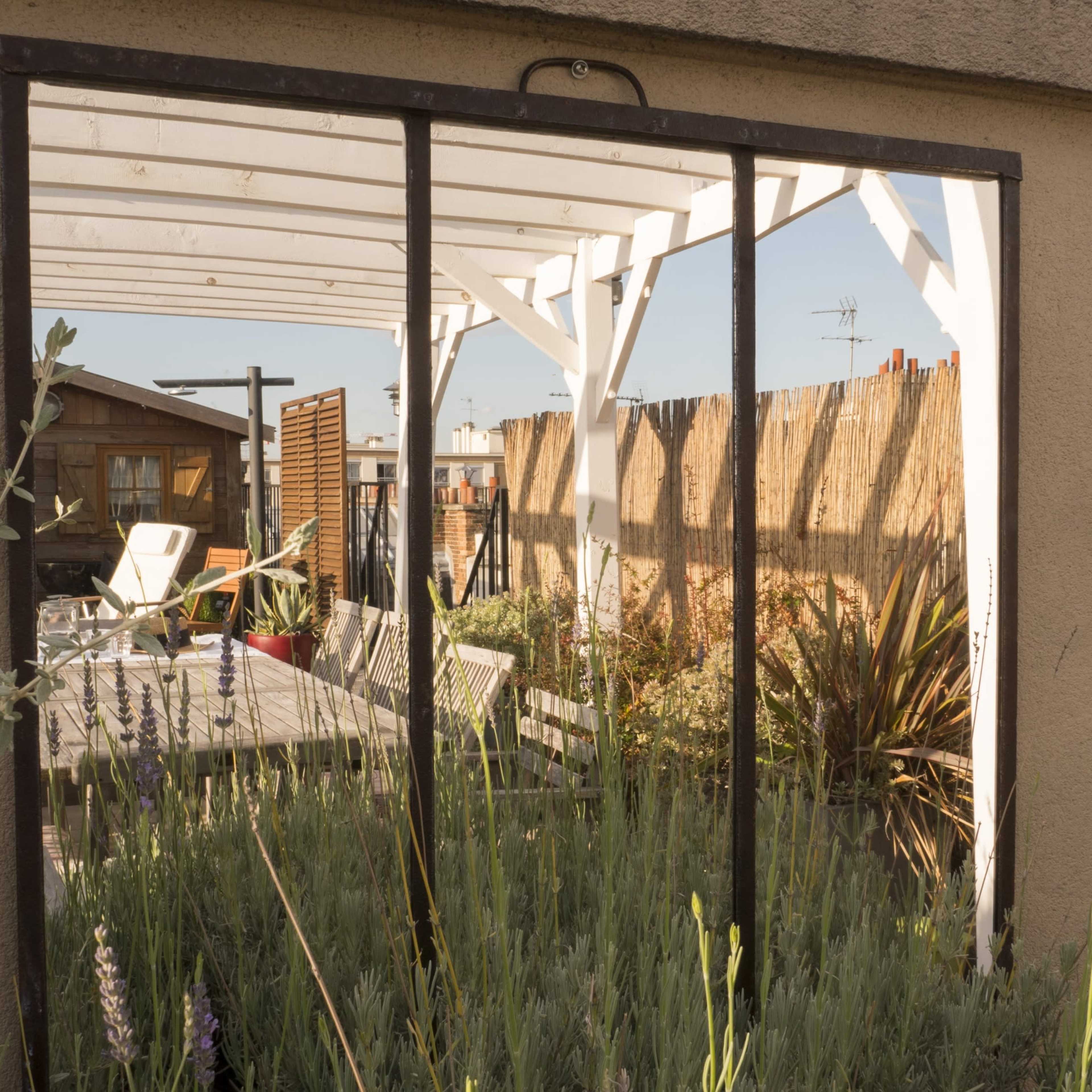A reflective mirror frame showcases a garden area with outdoor furniture and plants behind a wall.