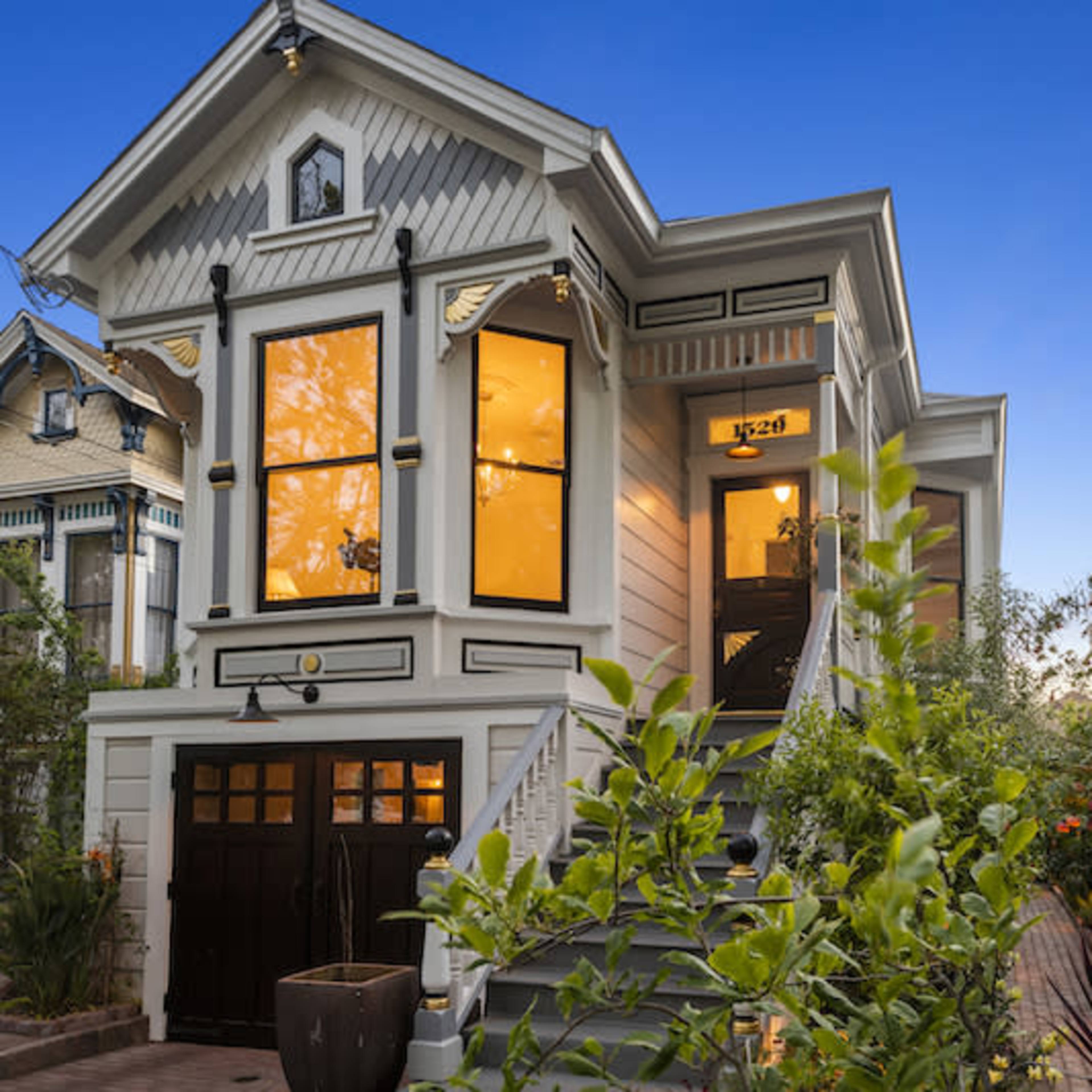 A Victorian-style house with large windows and a landscaped front garden is illuminated by evening light.